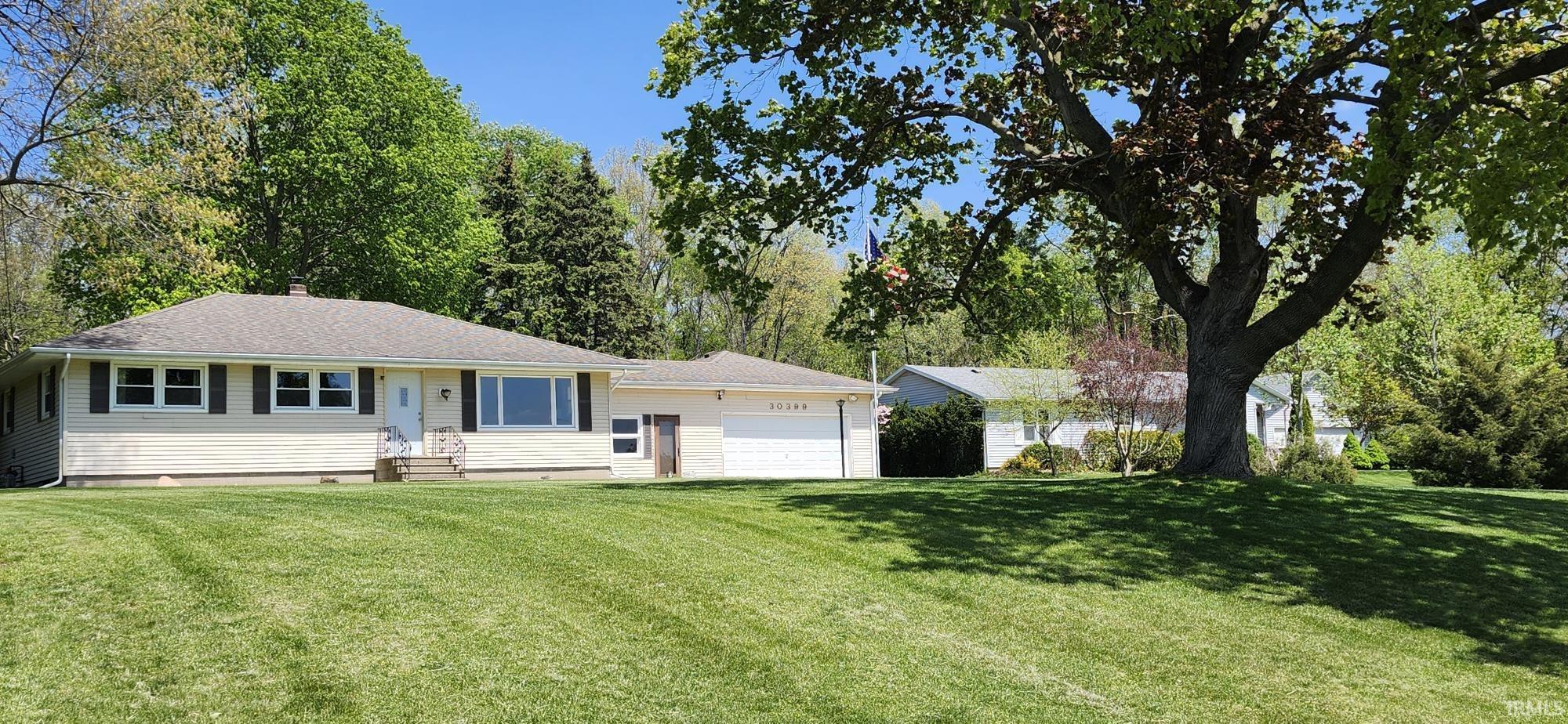 Ranch-style residence featuring a prominent front lawn, neutral-toned siding, dark window shutters, and a large picture window