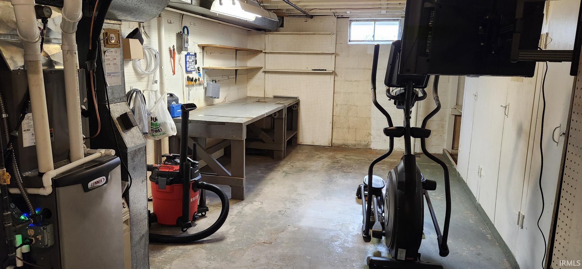 Unfinished basement space featuring a utility sink, built-in shelving, a workbench, and a casement window