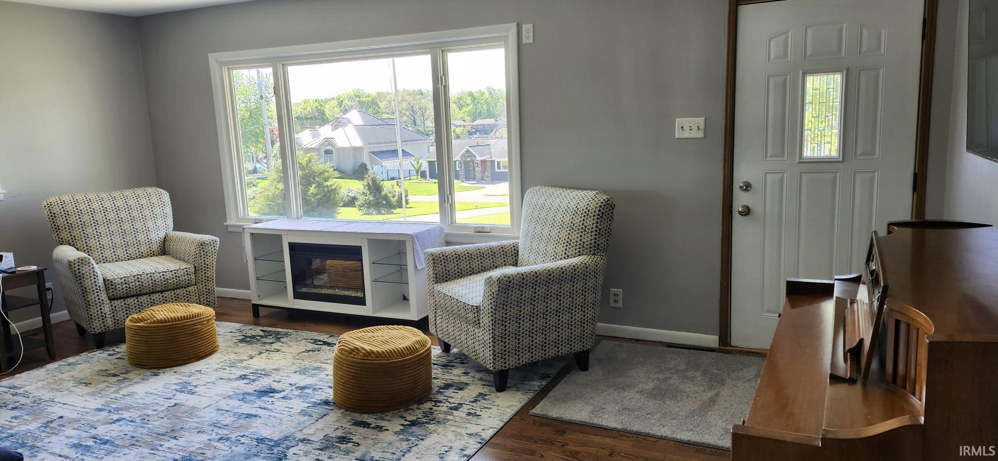 Light-filled living area featuring wood-finish flooring, a bright picture window, and a built-in media console with electric fireplace insert