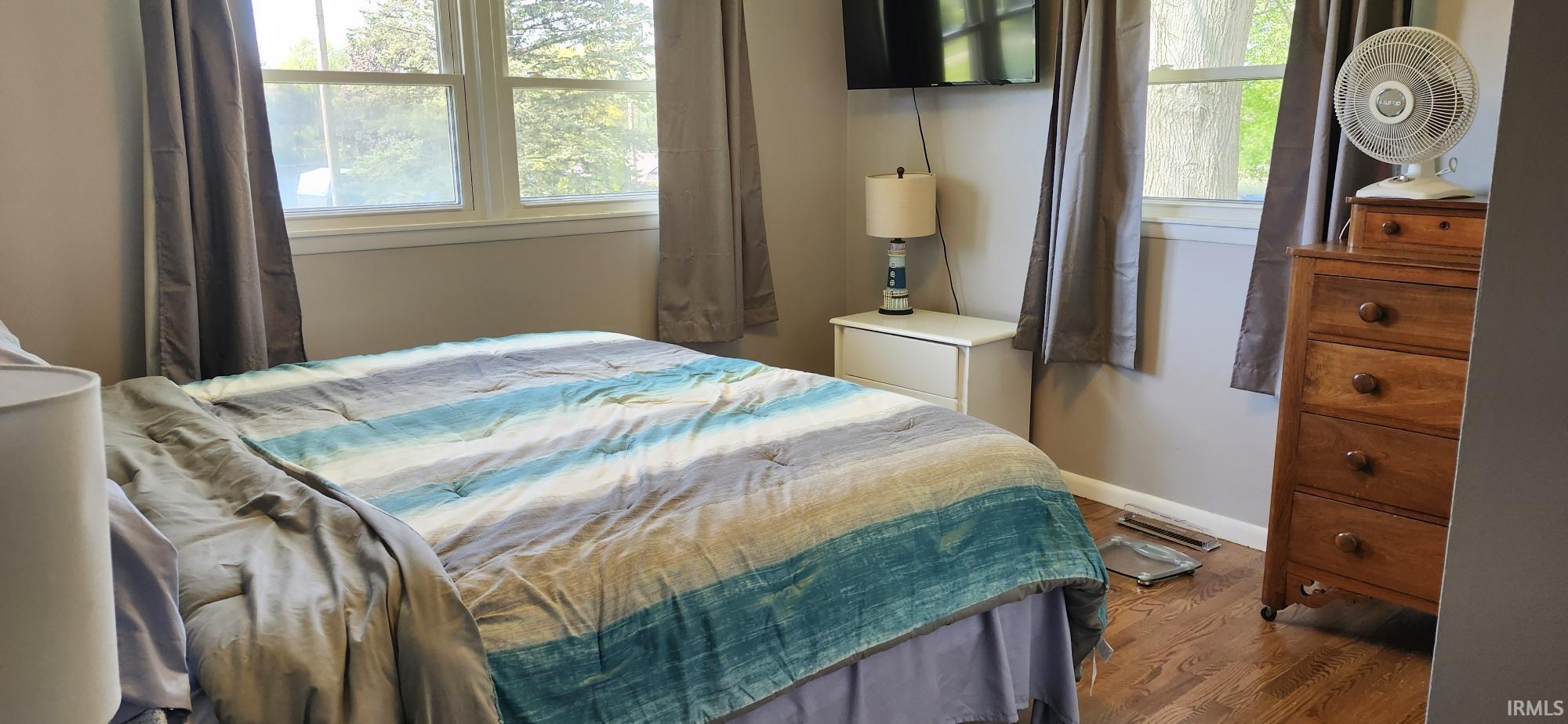 Bedroom featuring wood-finish flooring, two large windows with neutral drapes, and light gray wall paint