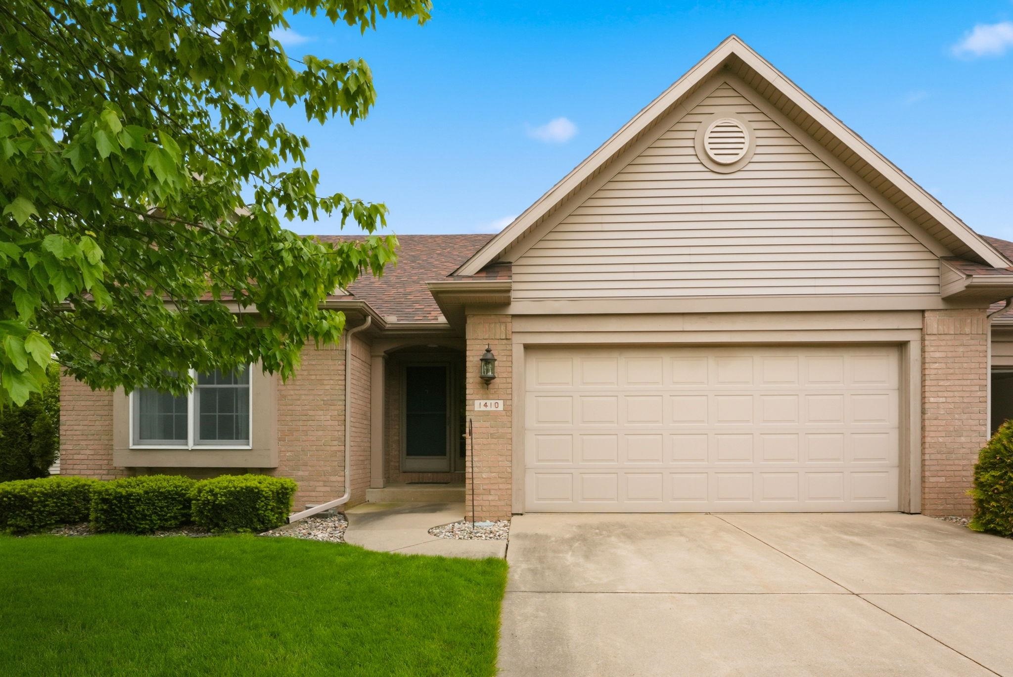Brick exterior with an attached garage, paved driveway, and mature landscaping