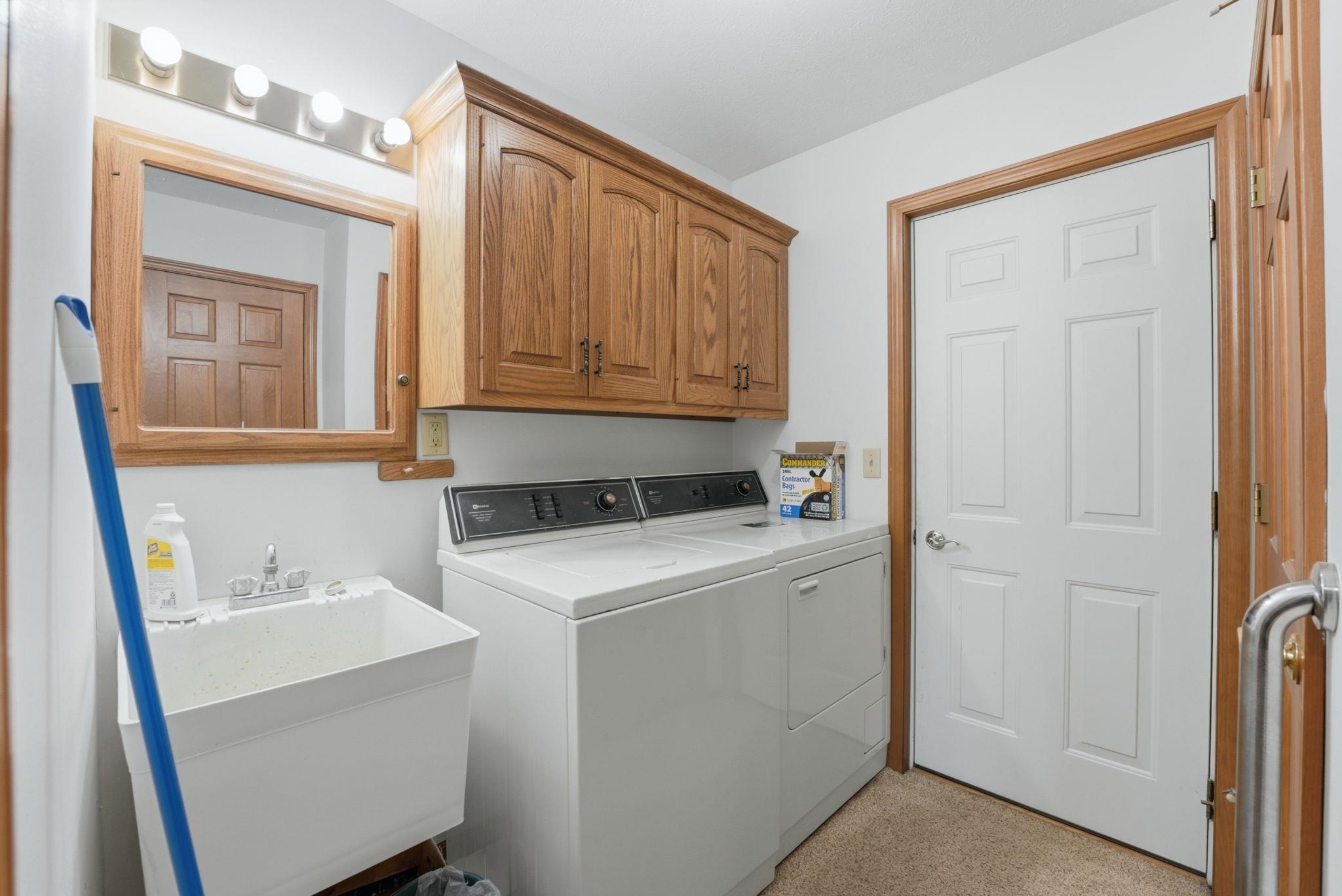 Dedicated laundry area featuring a utility sink with a chrome faucet, wood-finish cabinetry, and neutral wall paint