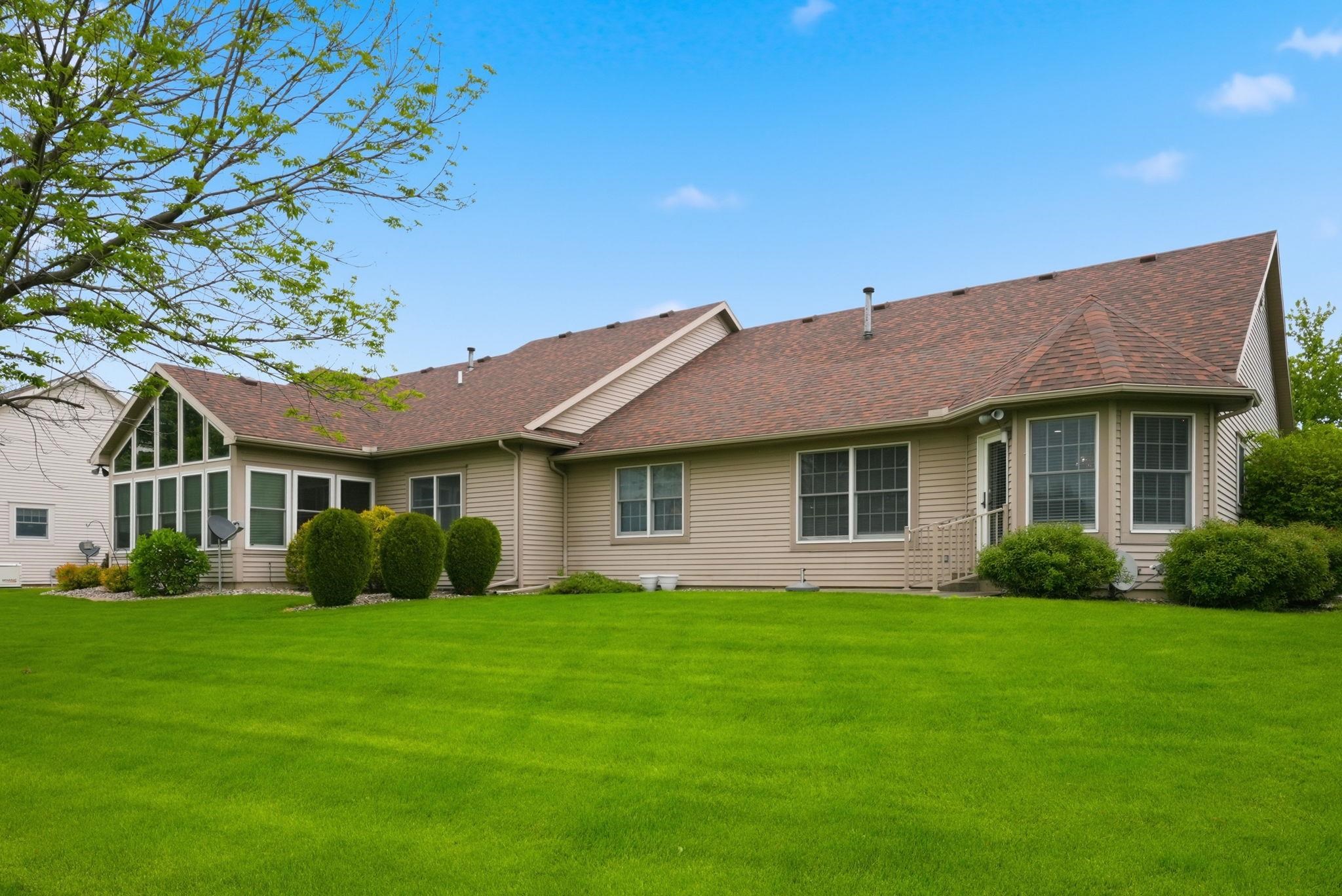 Expansive green lawn bordering a beige-sided residence with a brown shingle roof