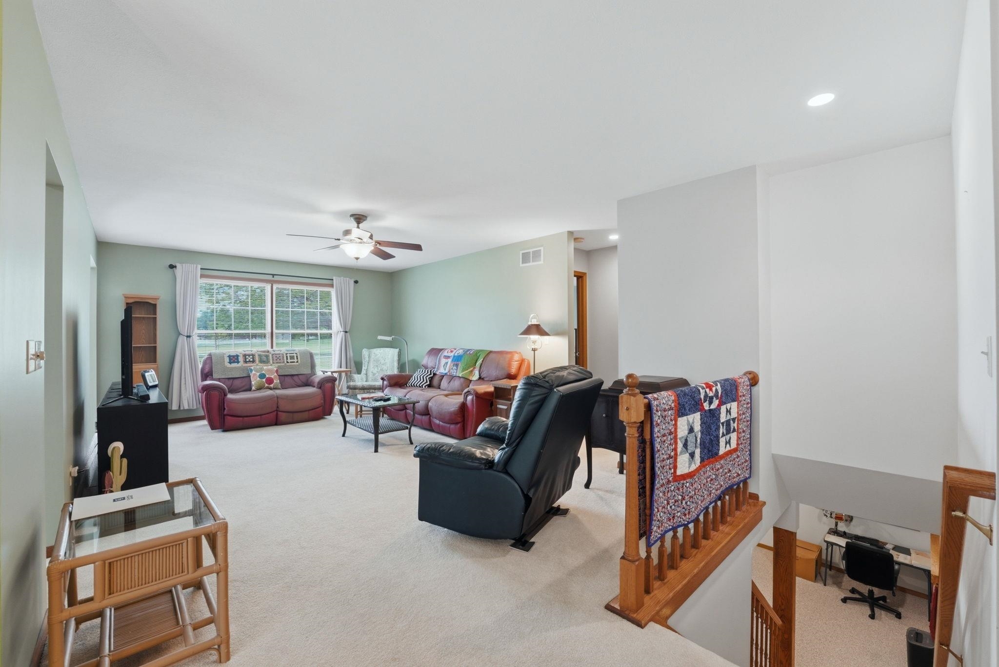 Carpeted living area featuring light green walls, a ceiling fan with integrated lighting, and a large window with white curtain panels