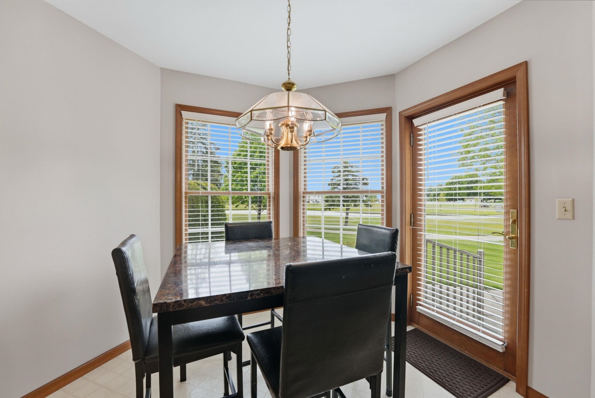 Corner dining area featuring multiple windows with blinds, a glass-paneled door with blinds, and a brass-finish chandelier