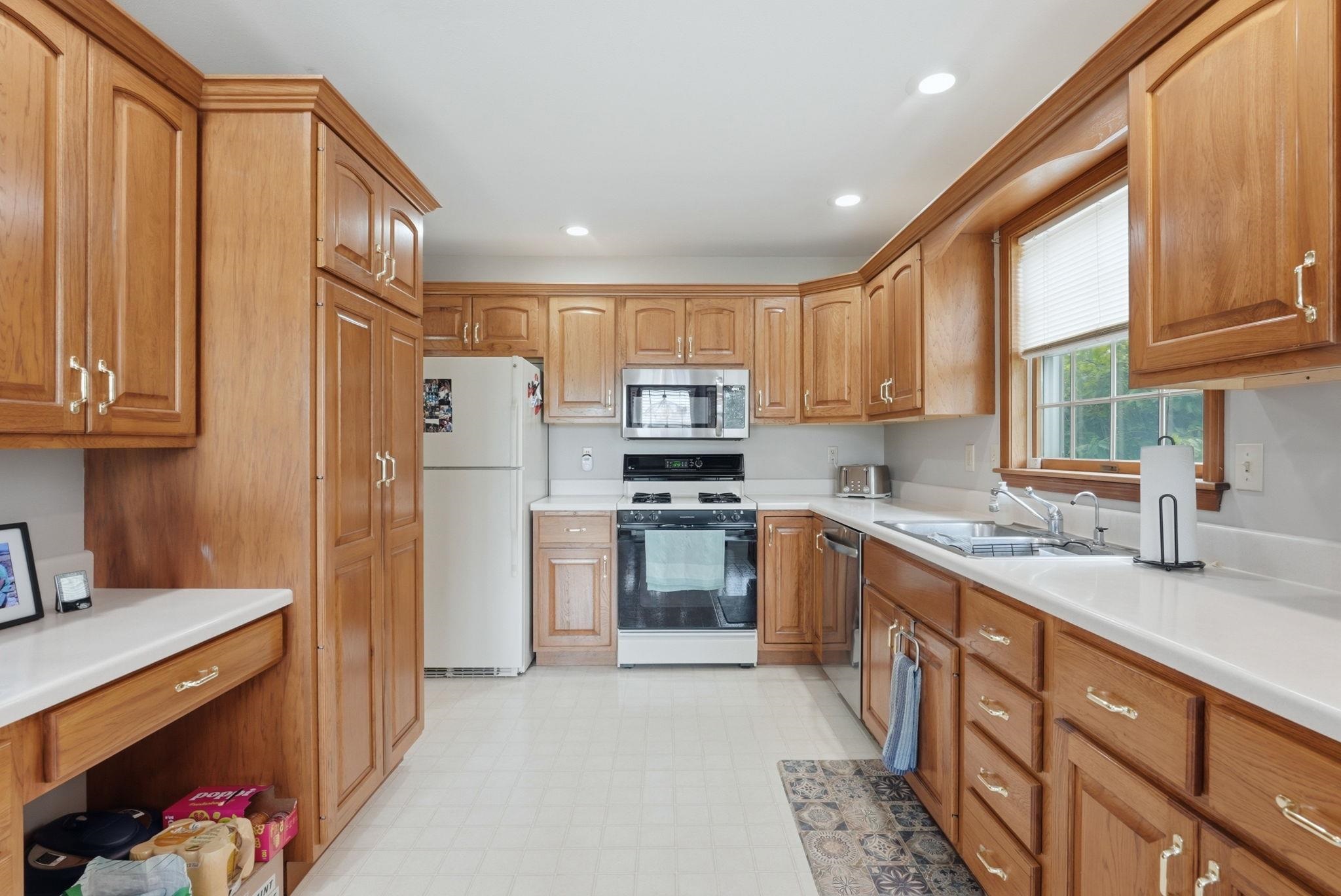 Kitchen featuring extensive wood cabinetry, white countertops, built-in stainless steel microwave, and white appliances