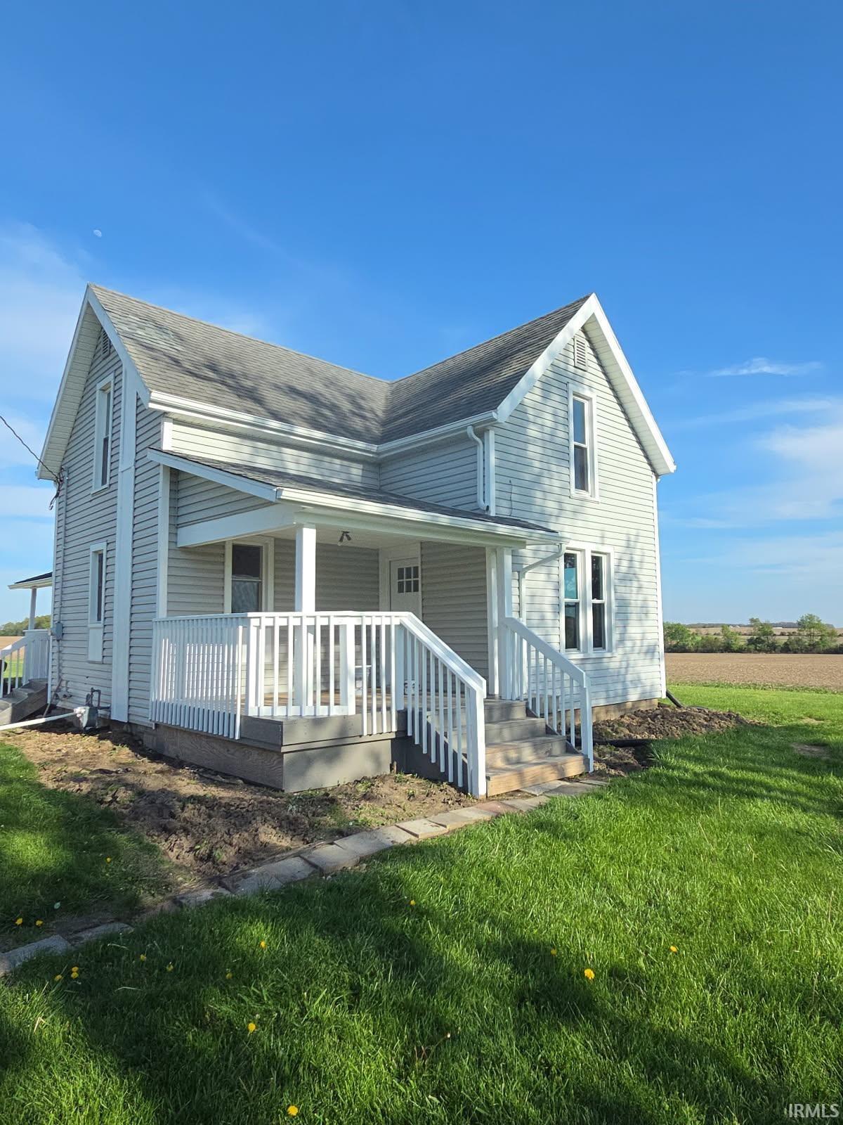 Traditional two-story residence featuring light-colored siding, a covered front porch, white railings, and a shingled roof