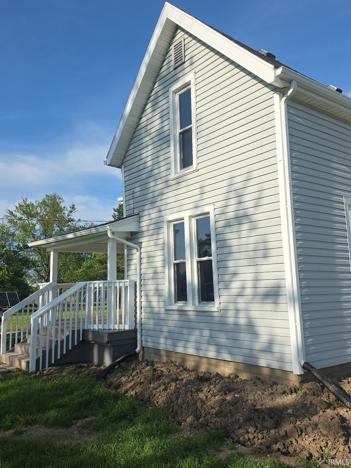 Light-colored horizontal siding exterior featuring a covered porch with white railings, white window trim, and a gabled roofline