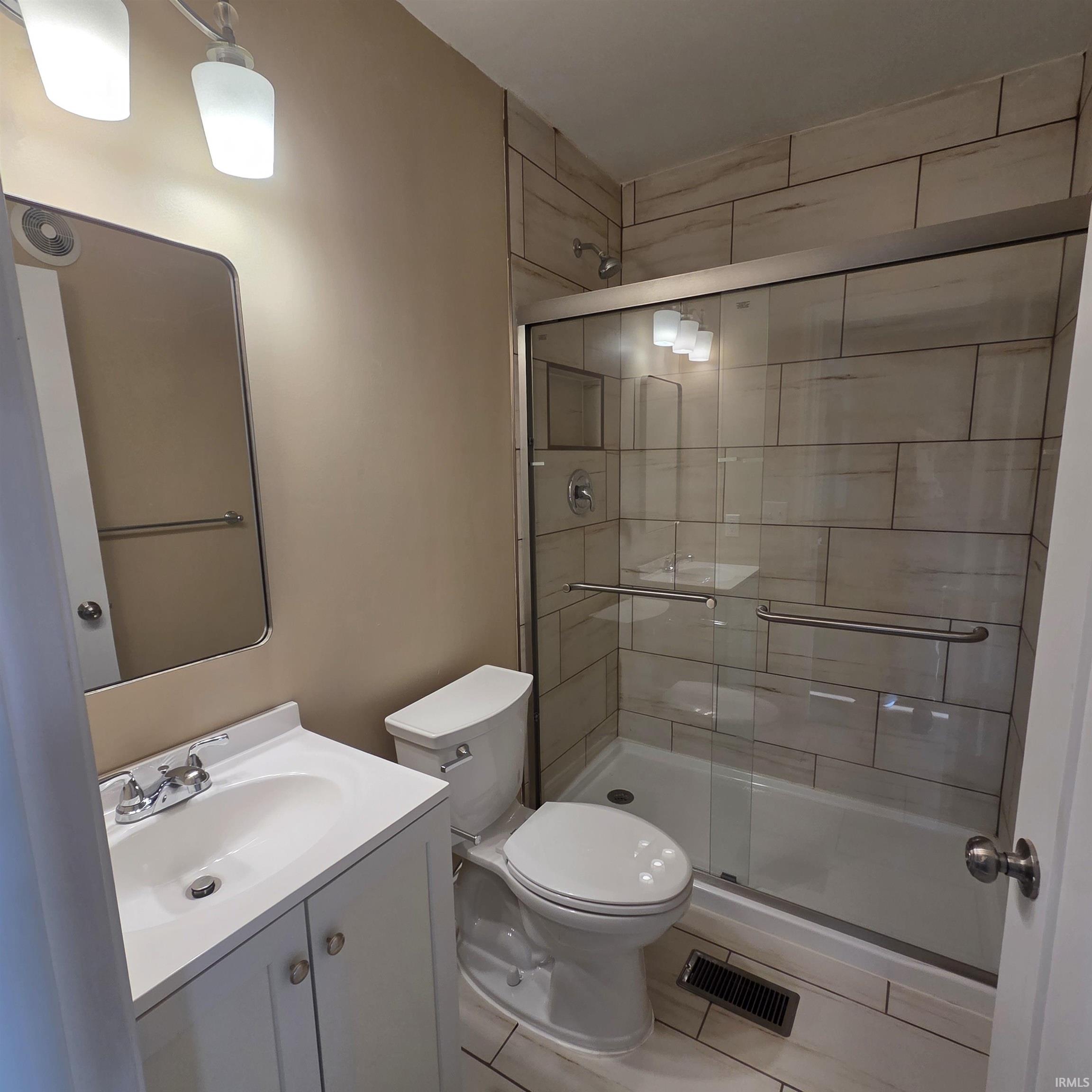 Bathroom featuring a glass-enclosed shower with subway tile surround, a white vanity with integrated sink, chrome fixtures, a wall-mounted mirror, and a white toilet