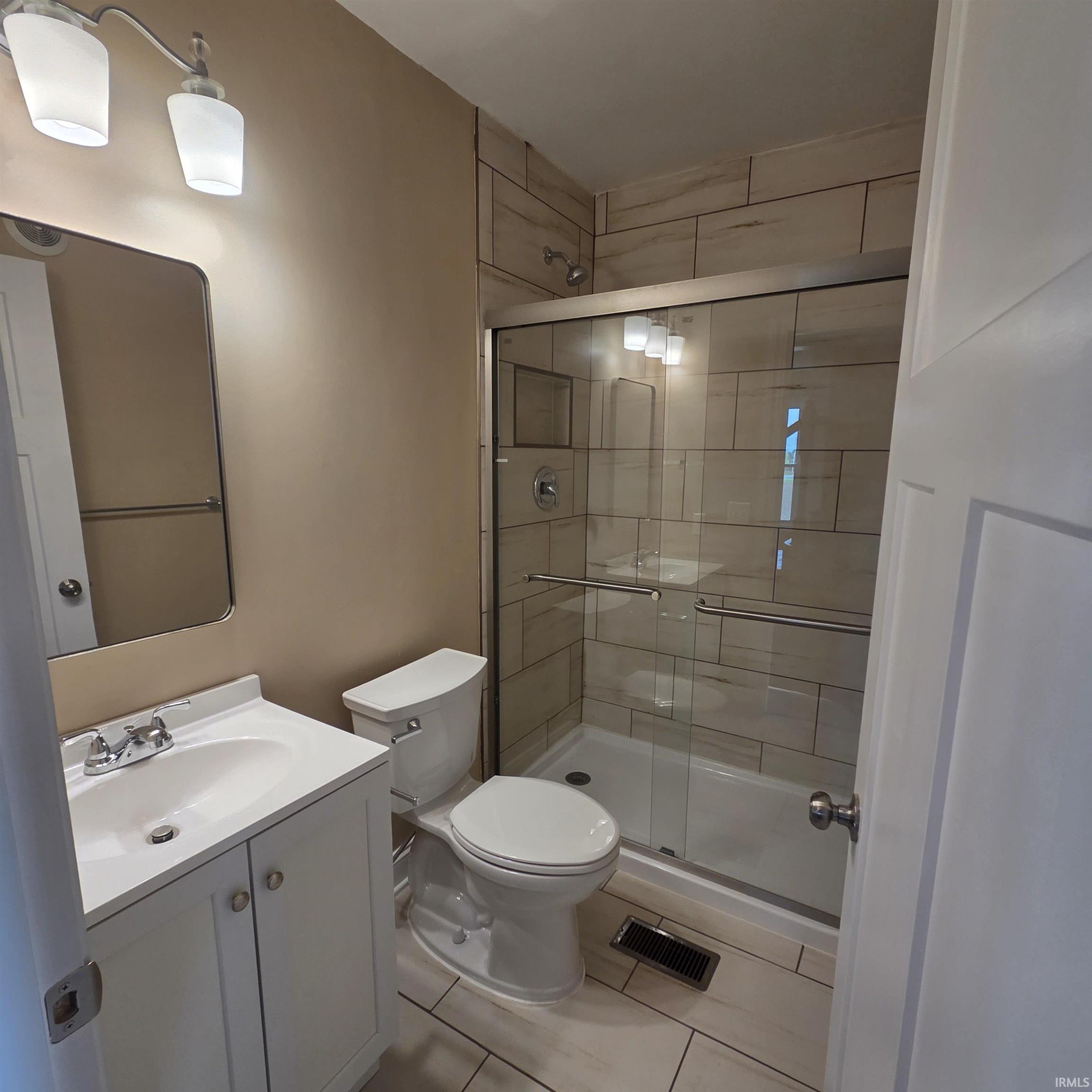 Bathroom featuring a glass-enclosed shower with tile surround, white vanity with integrated sink, chrome fixtures, and complementary floor tiling