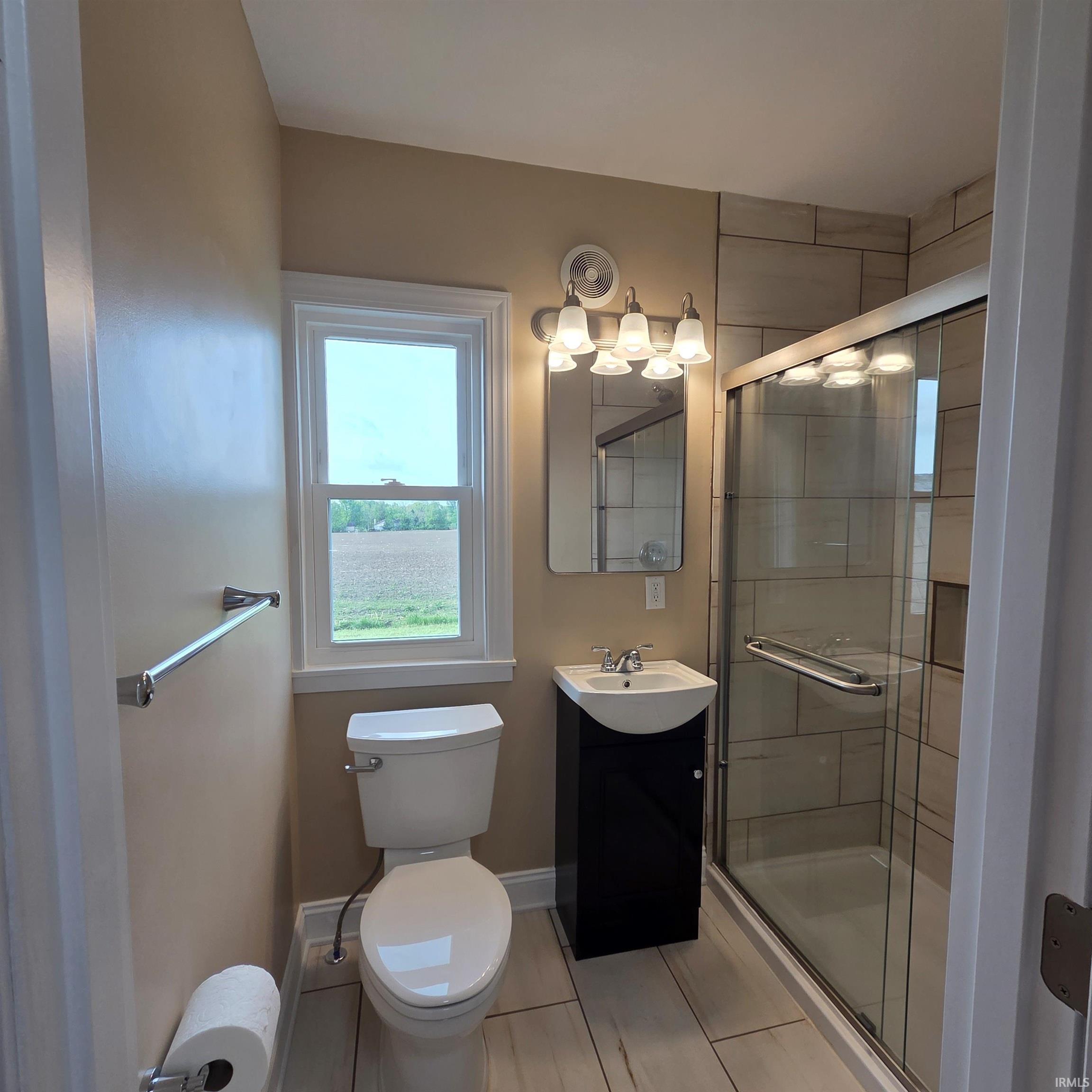 Contemporary bathroom featuring a black vanity with a vessel sink, a walk-in shower with clear glass enclosure and tiled walls, a rectangular mirror, and a window with white trim