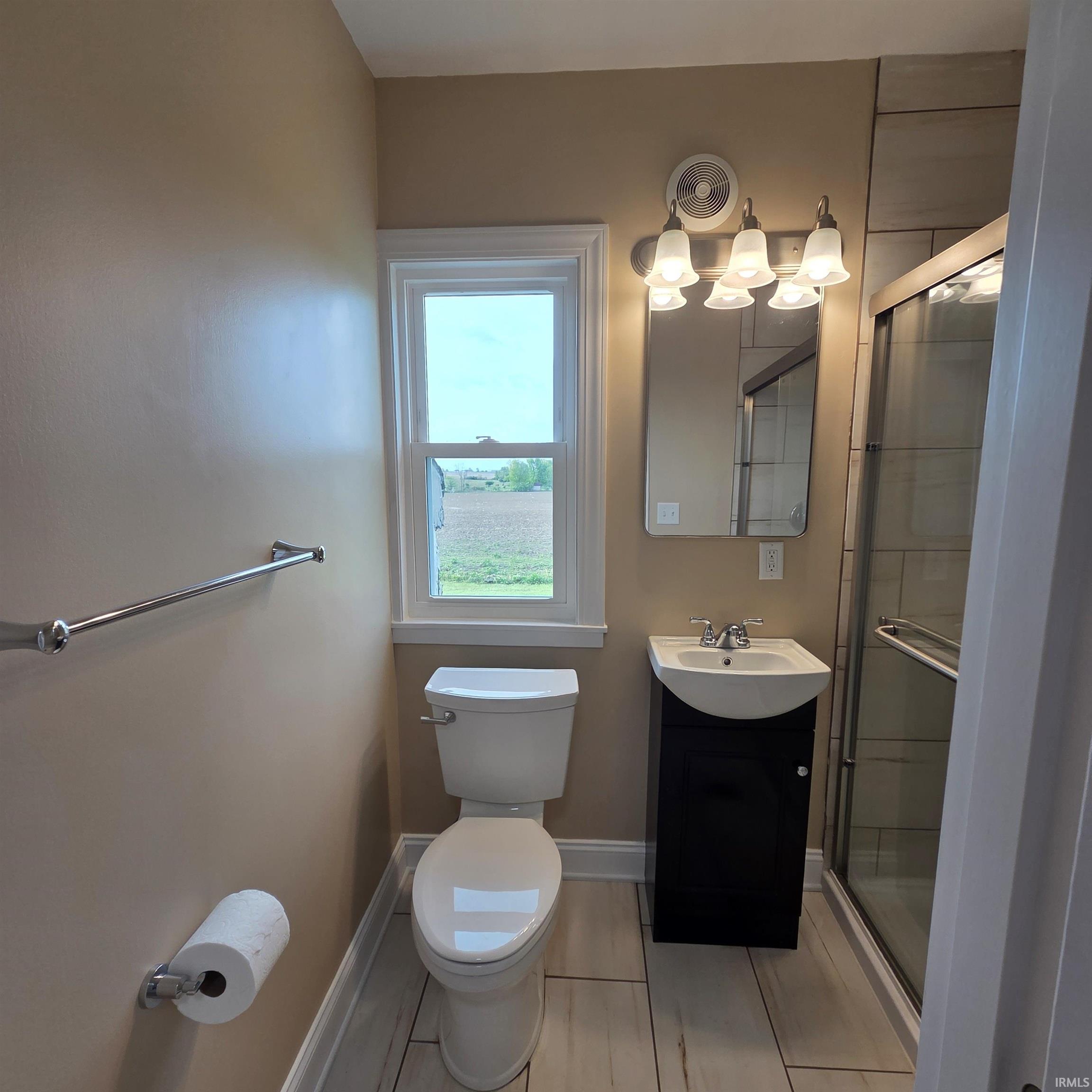 Bathroom featuring a window, white toilet, dark wood-finish vanity with an integrated sink, polished chrome faucet, and a glass-enclosed shower