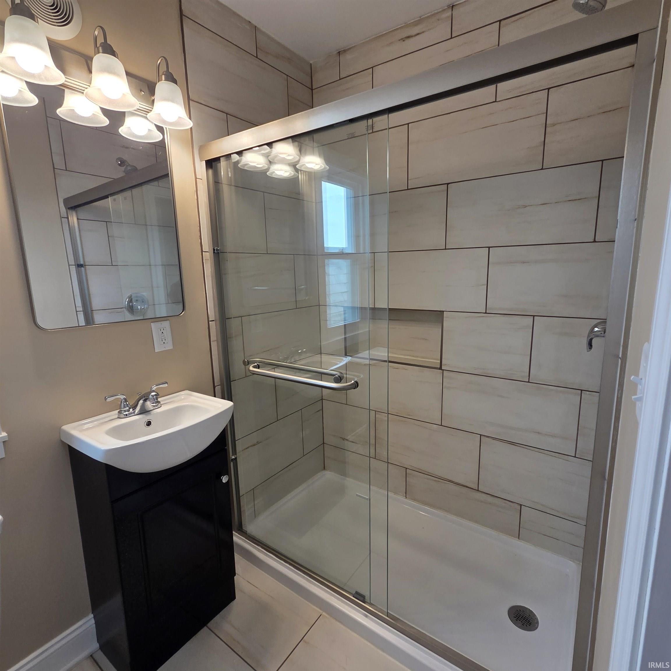 Glass-enclosed shower with subway tile surround and integrated shelf, paired with a contemporary vanity featuring a ceramic sink