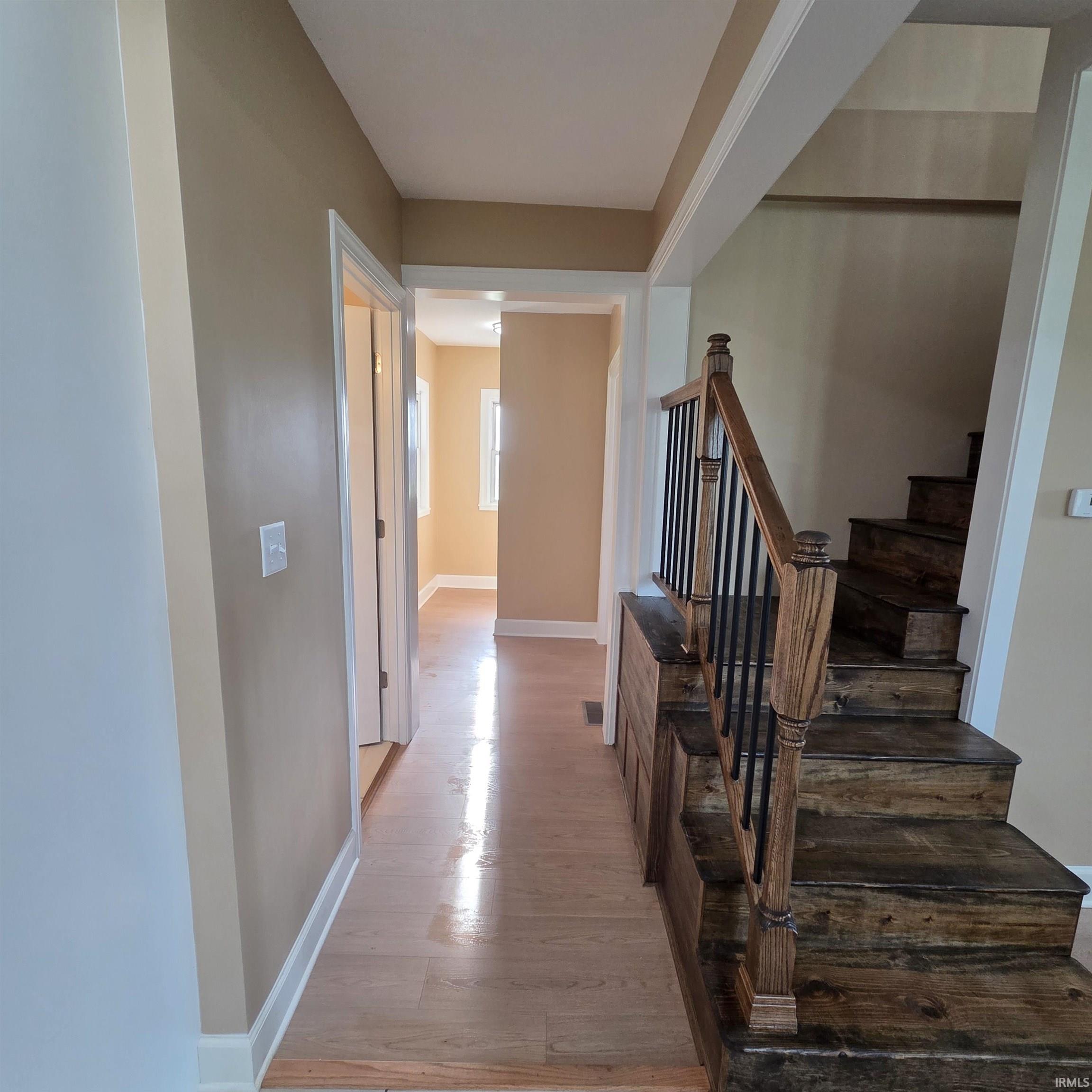 Staircase entry featuring wood-finish treads, black metal balusters, and a wood-finish newel post