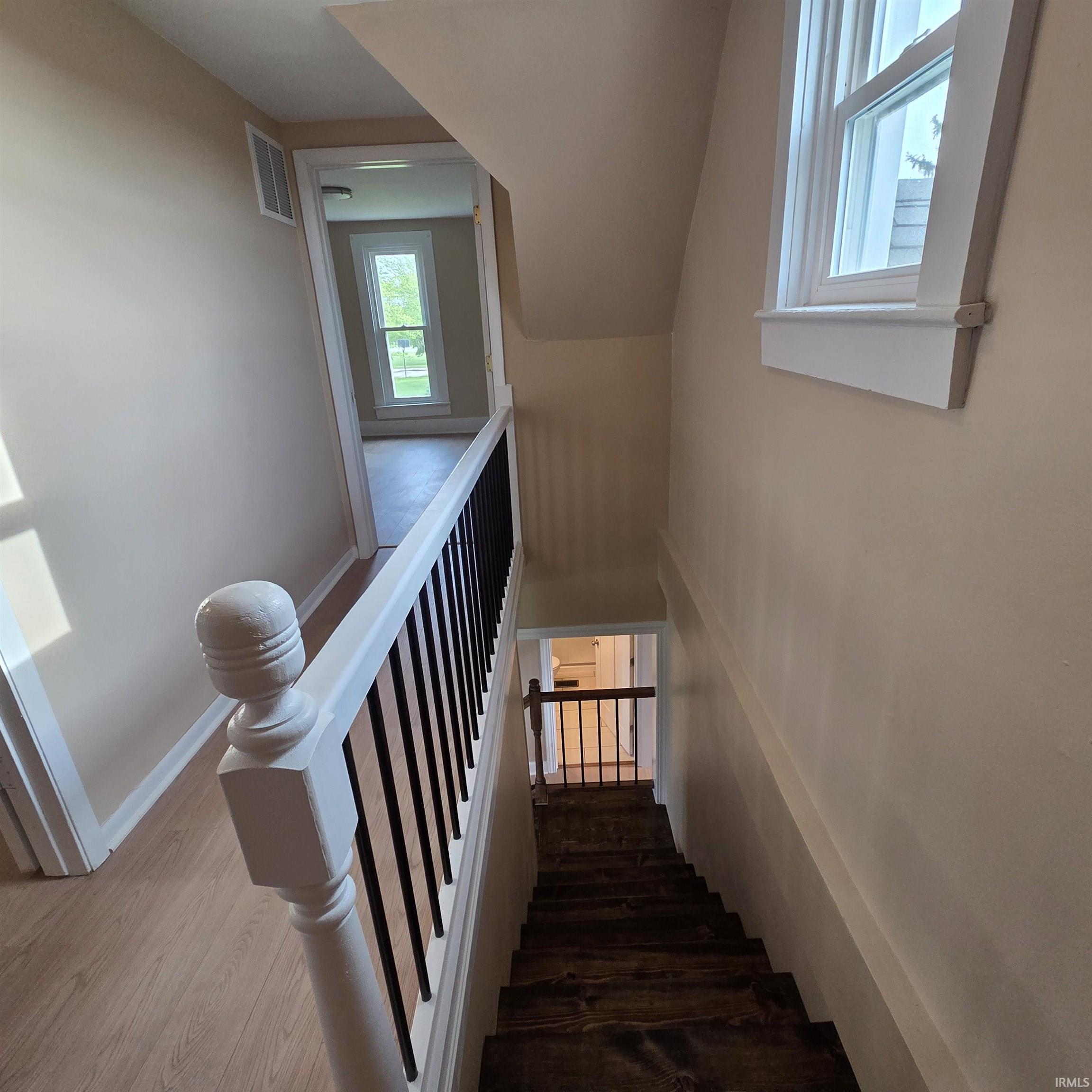 Stairwell featuring wood-finish treads, a white newel post, and black balusters