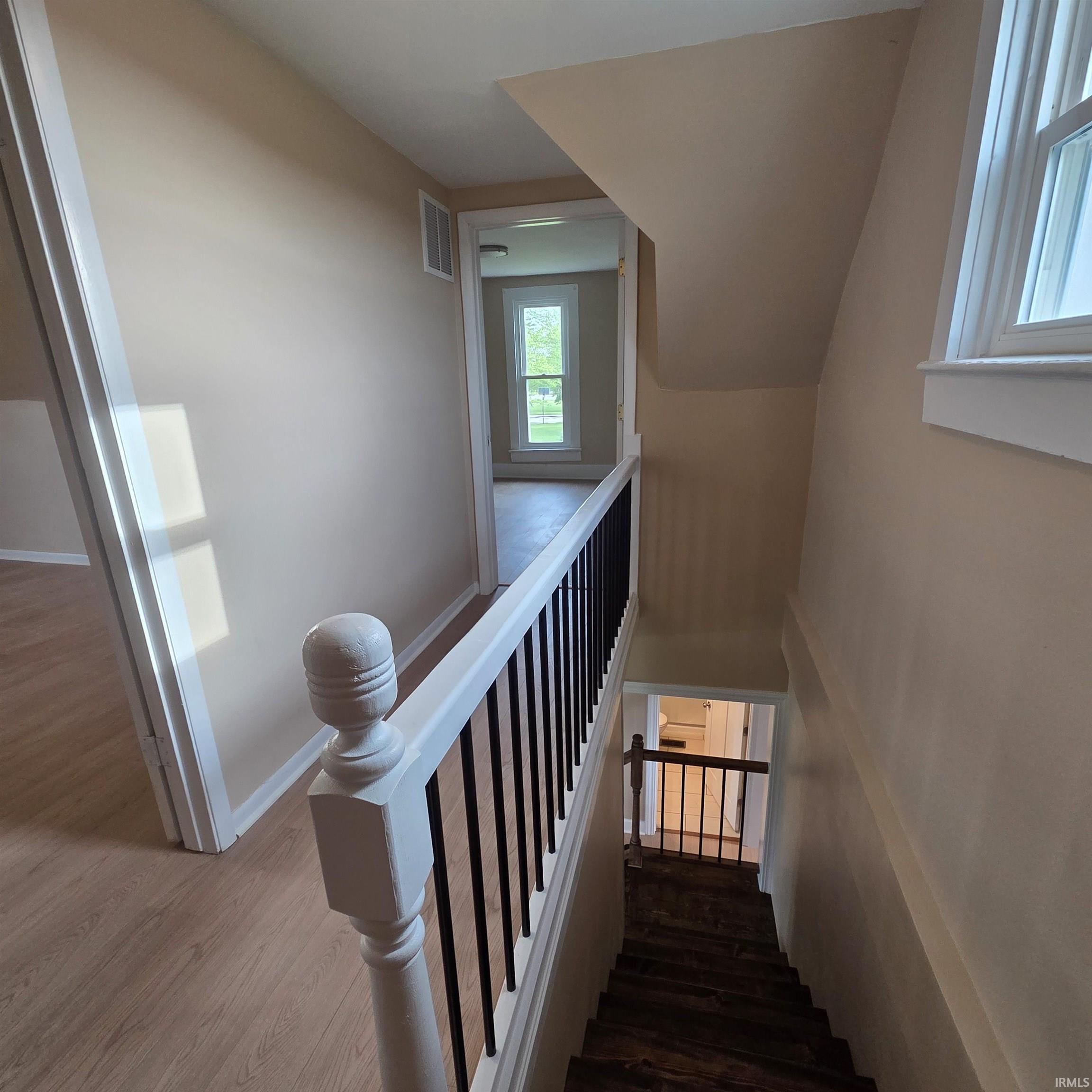 Staircase with wood-finish treads and risers, featuring a white painted newel post and balustrade with black metal spindles