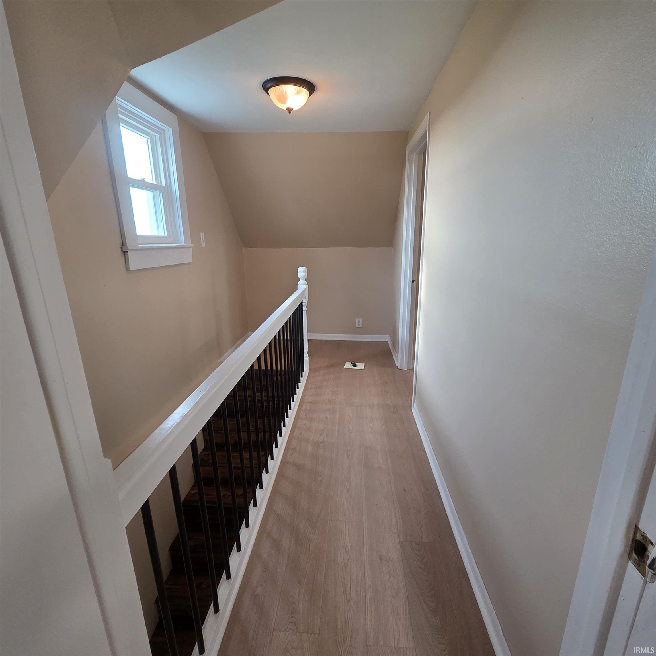 Upper-level hallway featuring wood-finish flooring, a white-framed window, and a staircase with a white railing and dark balusters