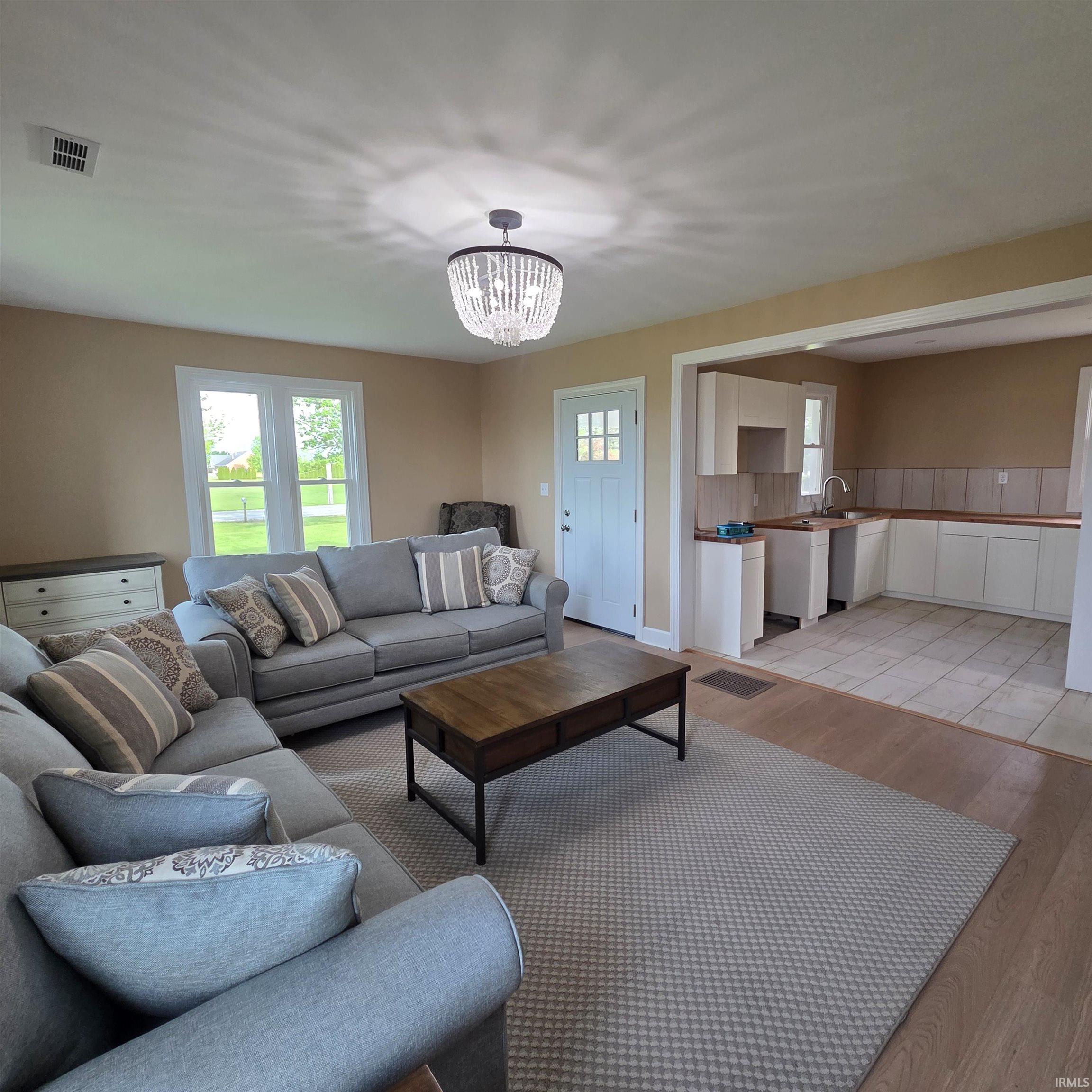 Open-concept living space featuring wood-finish flooring, a crystal chandelier, and a white paneled door with window accents