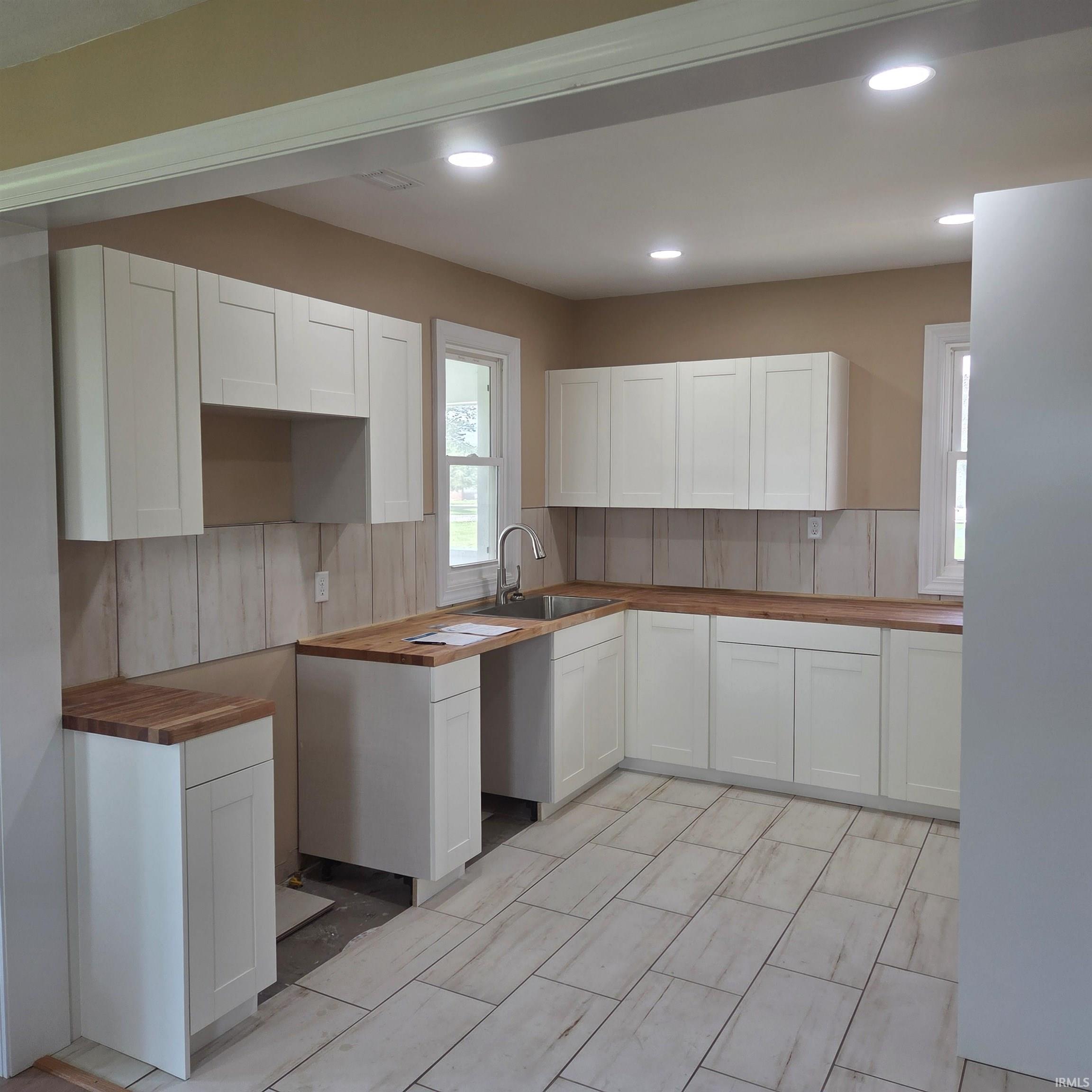 Kitchen featuring white shaker-style cabinetry, wood-finish countertops, and a stainless steel sink with a gooseneck faucet