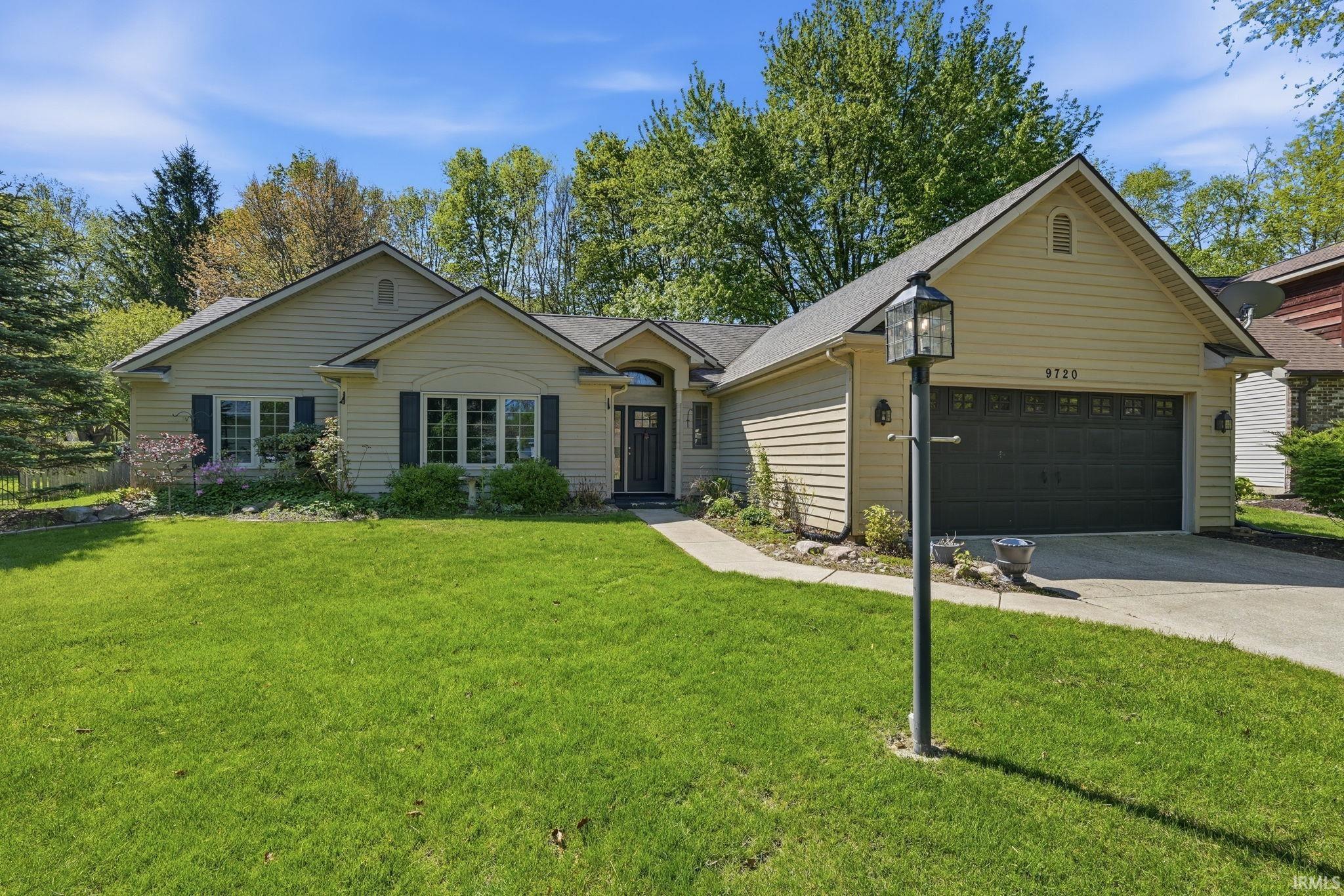 Ranch-style residence featuring light-colored siding, a dark asphalt shingle roof, and a two-car garage with a dark door