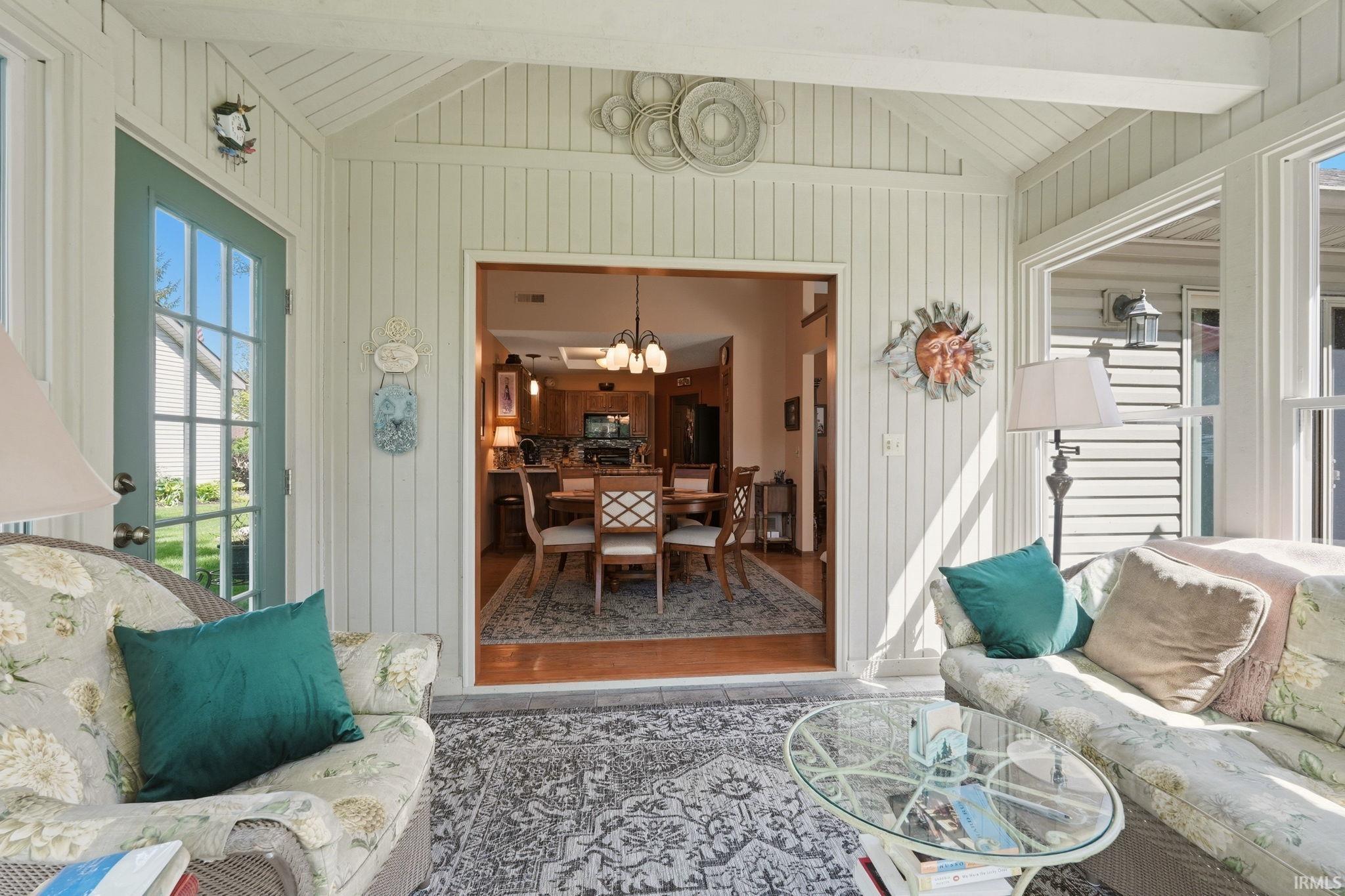 Sunroom featuring vertical paneling, exposed ceiling beams, and a light blue paneled door with windowpanes