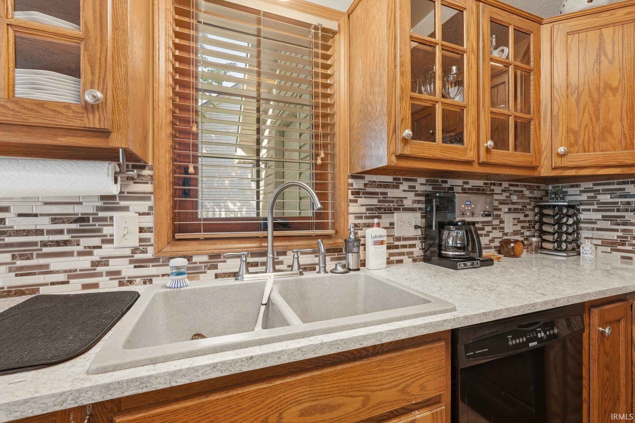 Kitchen featuring a double basin sink with a chrome faucet, light-toned countertops, and a mosaic tile backsplash