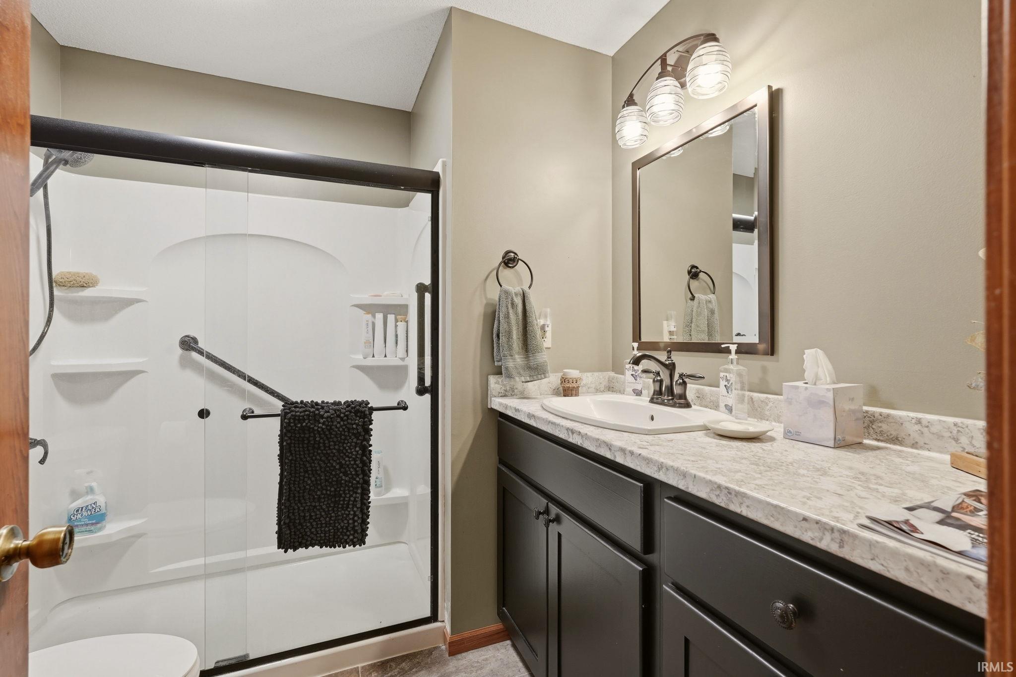 Bathroom featuring a bathtub with a clear glass sliding door, integrated shelving, and a dark-finished grab bar