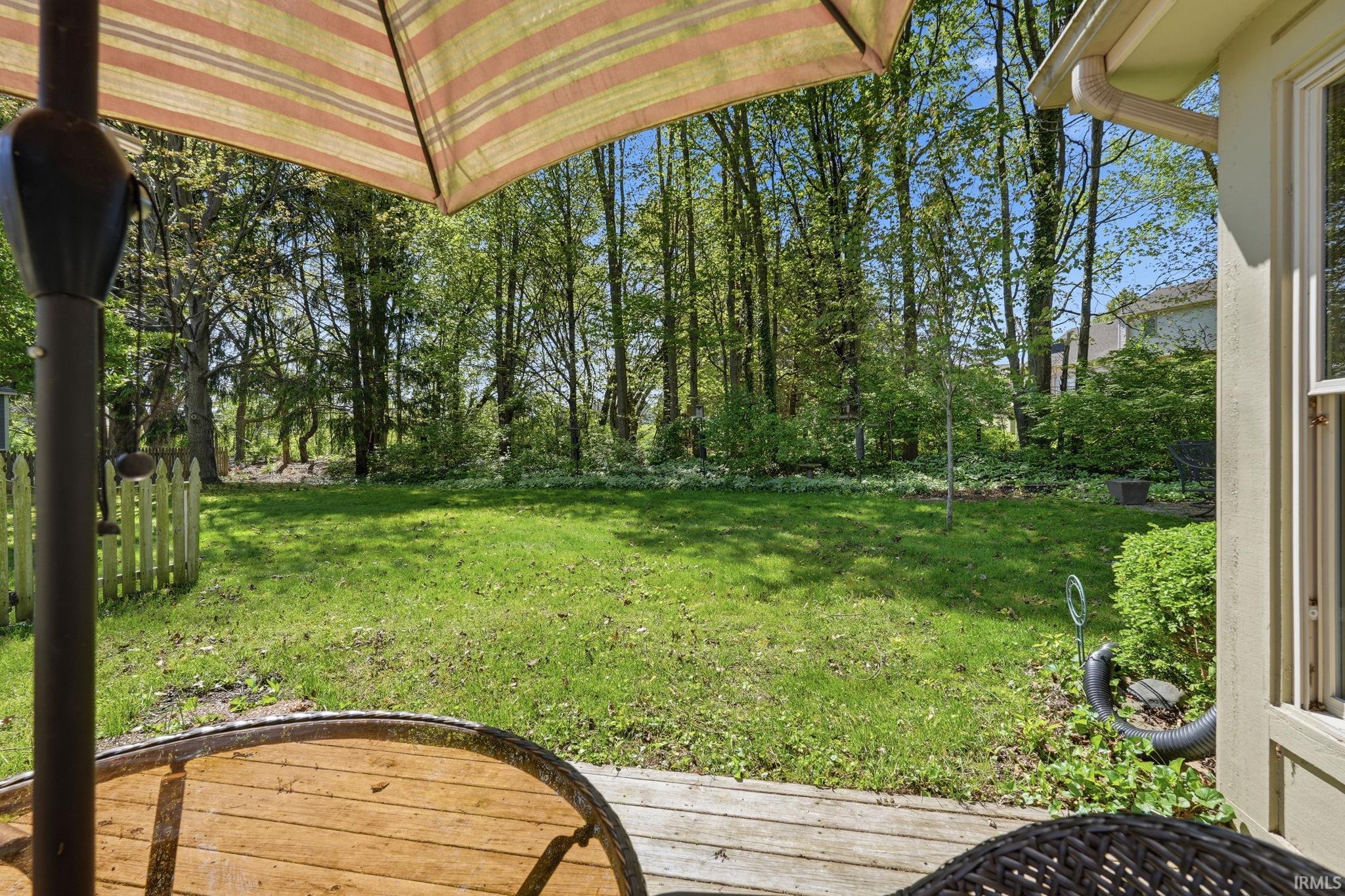 Expansive green lawn surrounded by mature trees, featuring a wooden picket fence and a wooden deck