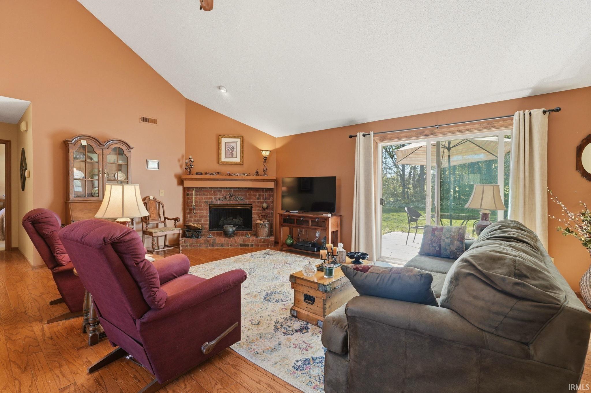 Living area featuring wood-finish flooring, a vaulted ceiling, and a brick fireplace with a wood mantle