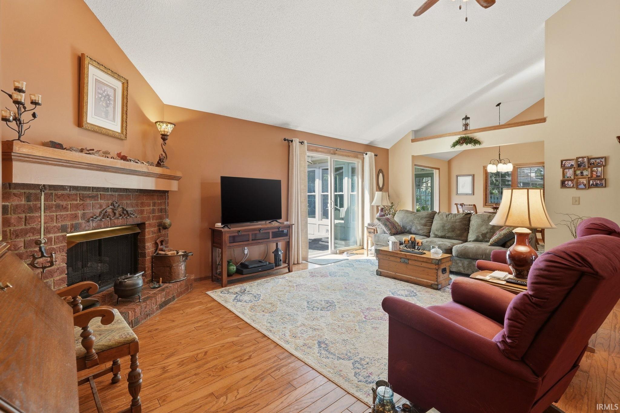 Spacious living area featuring vaulted ceilings, wood-finish flooring, and a brick fireplace with mantel