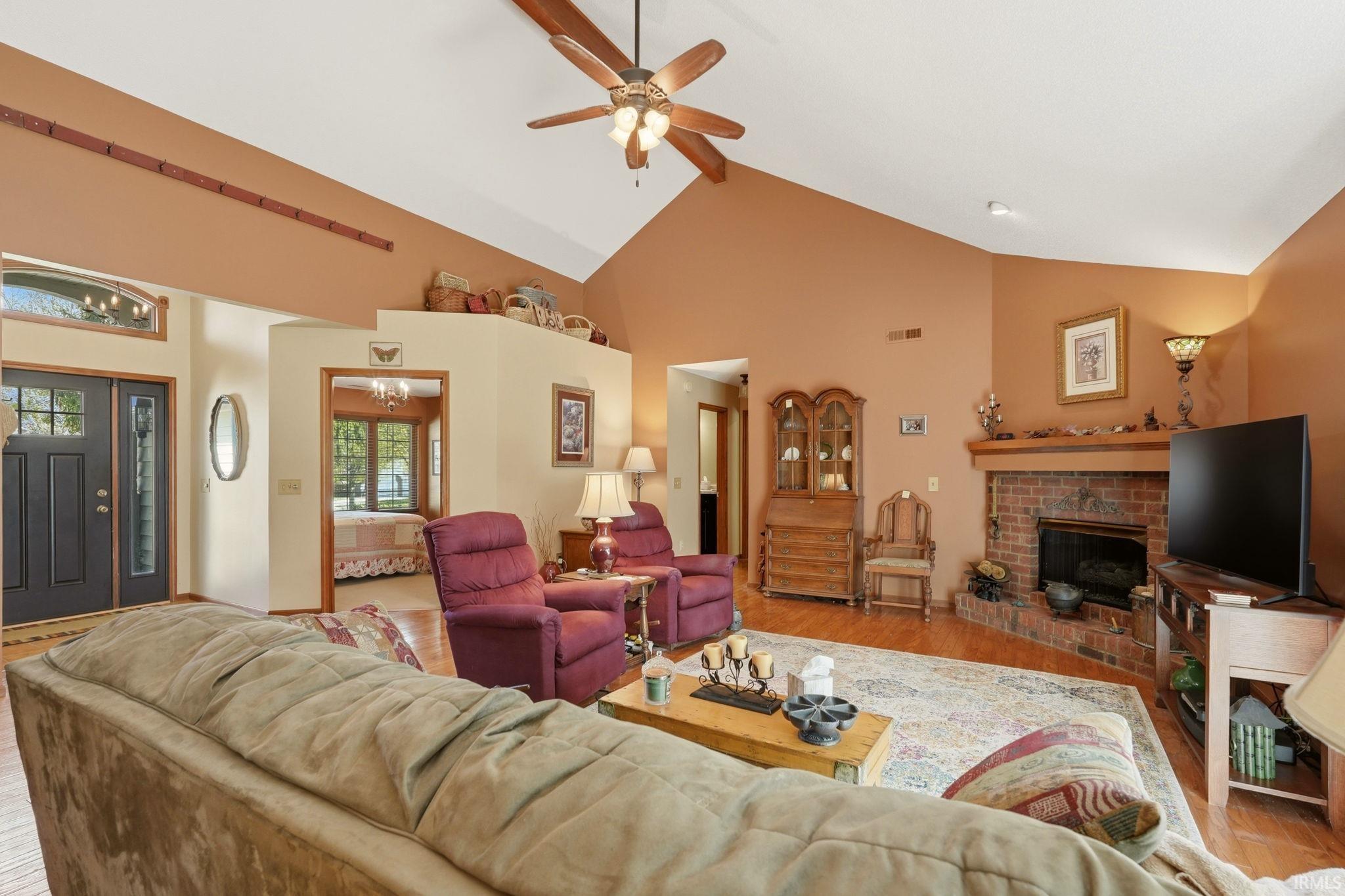 Vaulted ceilings featuring a ceiling fan and recessed lighting, a brick fireplace with a wood mantle, wood-finish flooring, and a double entry door with decorative glass inserts and transom window
