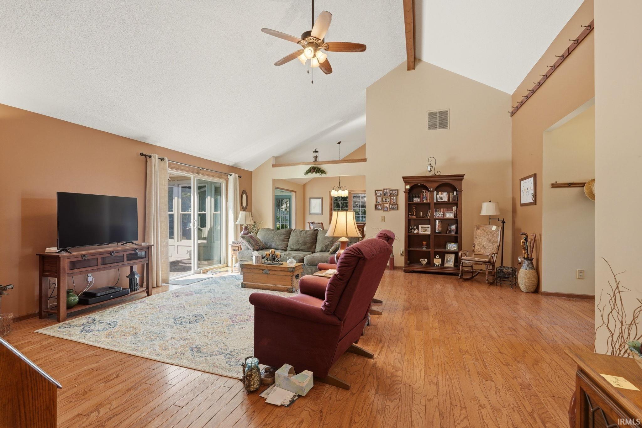 Spacious living area featuring vaulted ceilings with exposed wood beams, wood-finish flooring, and a ceiling fan