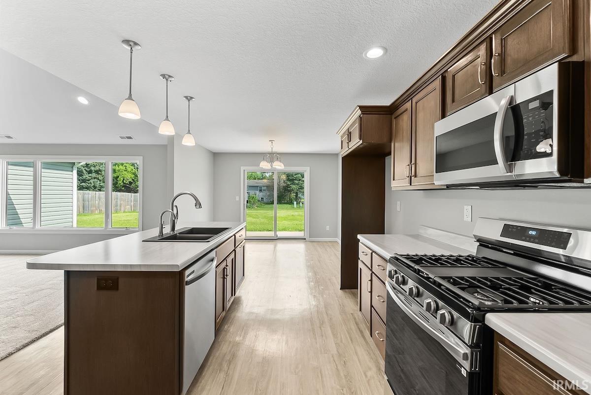 Kitchen featuring an expansive island with a double basin sink, stainless steel appliances, wood-finish cabinetry, and light-toned countertops