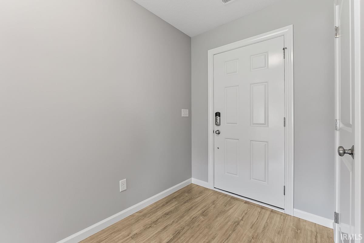 Entryway featuring a white six-panel door with a digital lock, light wood-finish flooring, and light gray painted walls with white trim