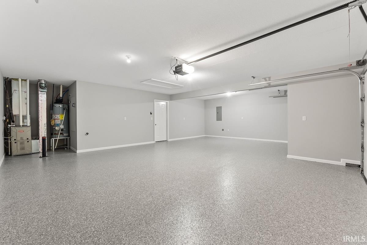 Spacious garage featuring a durable epoxy-coated floor, overhead lighting, a white pedestrian door, and a visible electrical panel