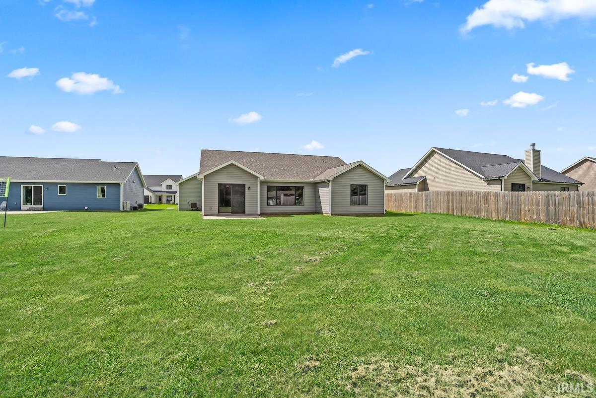 Spacious backyard featuring a substantial lawn area, a privacy fence along one perimeter, and a concrete patio