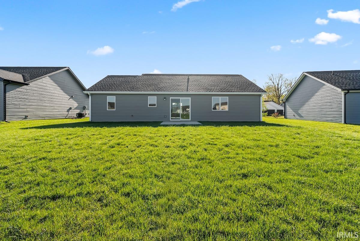 Spacious backyard featuring a large green lawn, a concrete patio, and a modern home exterior with gray siding