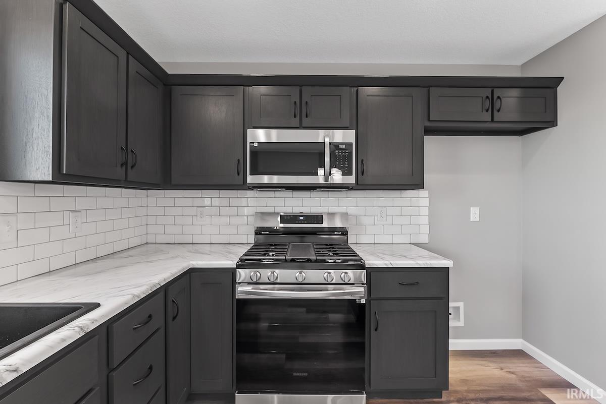 Modern kitchen featuring dark cabinetry, white subway tile backsplash, stainless steel range, built-in microwave, and wood-finish flooring