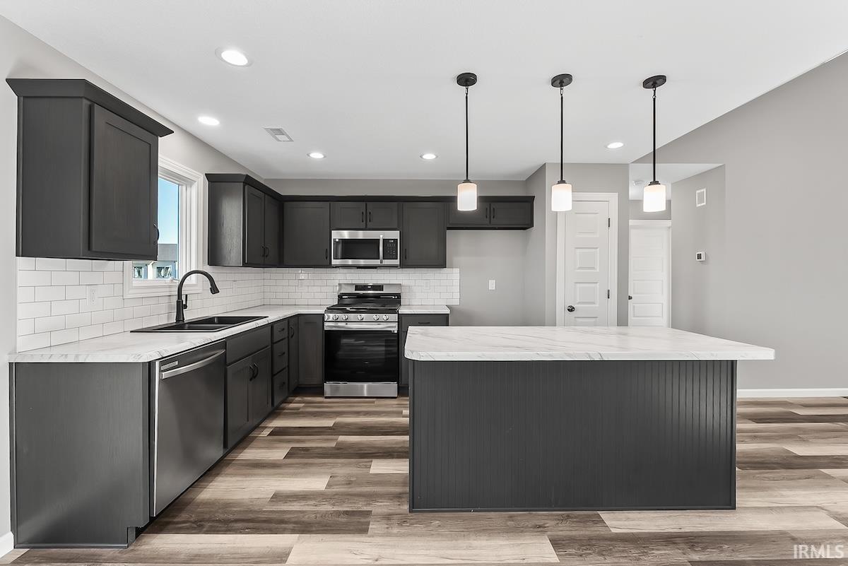 Modern kitchen featuring dark cabinetry, stainless steel appliances, white subway tile backsplash, and wood-finish flooring
