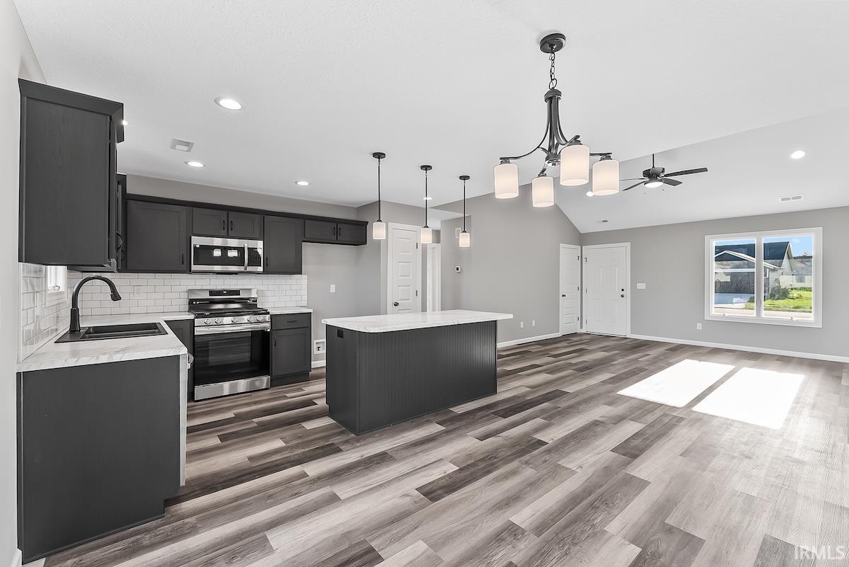 Open-concept living space featuring wood-finish flooring, a vaulted ceiling, and dark cabinetry