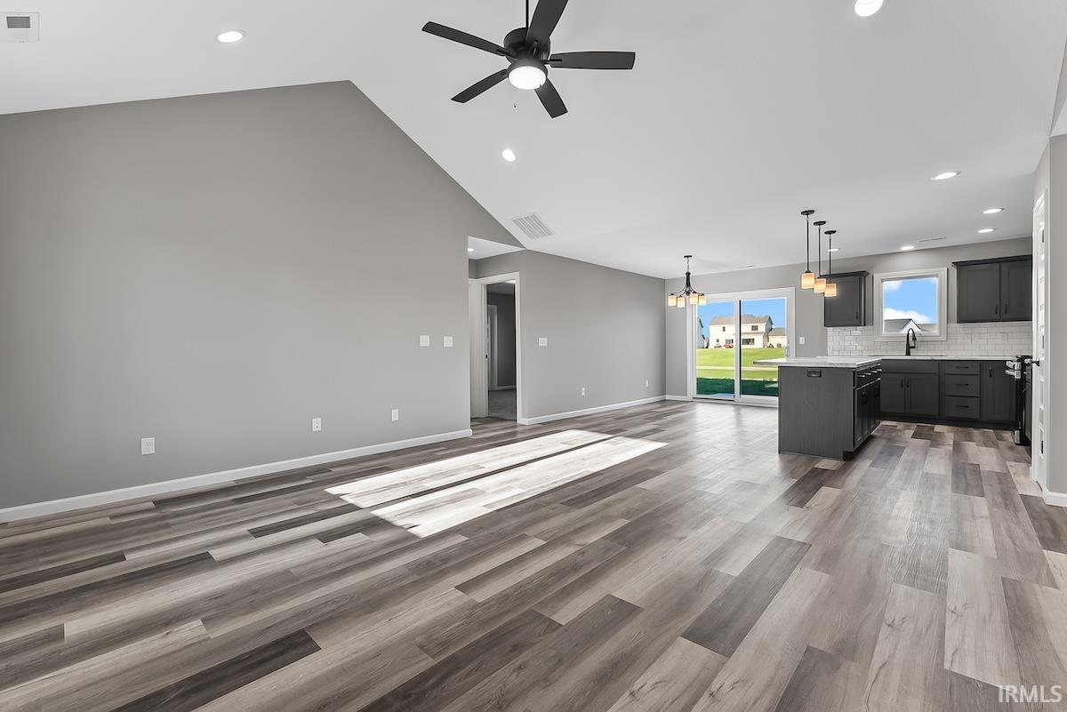 Spacious open-concept living area featuring vaulted ceilings, recessed lighting, and wood-finish flooring