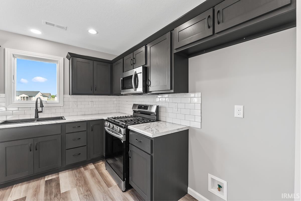 Kitchen featuring dark shaker-style cabinetry, white subway tile backsplash, and wood-finish flooring