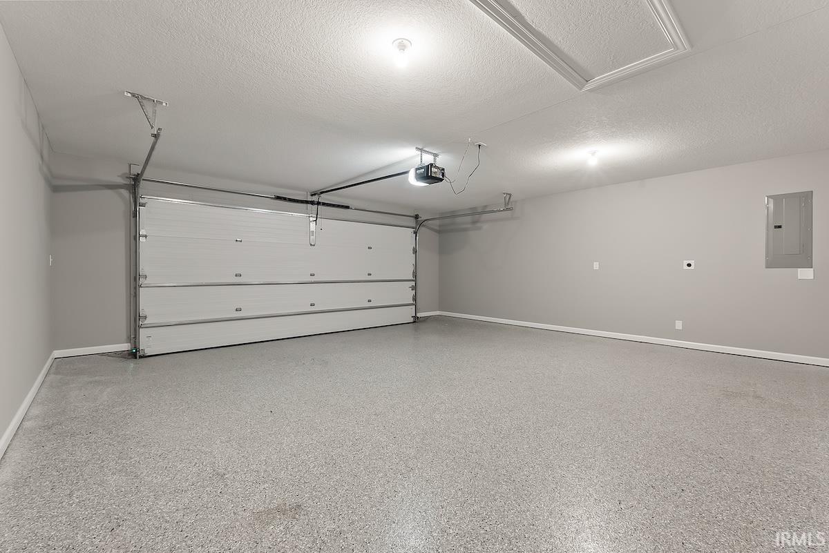 Spacious garage featuring a light gray speckled epoxy floor, white paneled garage door with automatic opener, and recessed lighting