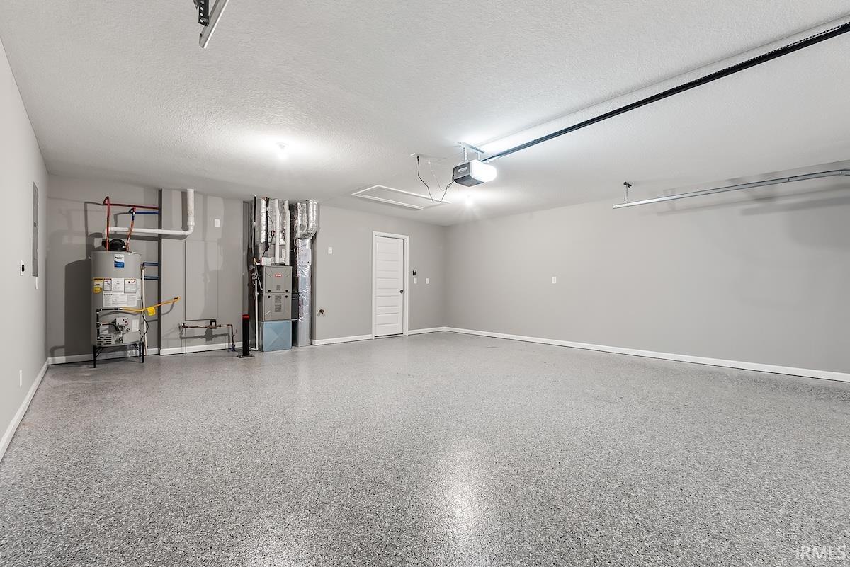 Spacious garage featuring a durable epoxy-coated floor, neutral gray walls, a white paneled door, ceiling-mounted lighting, and an attic access panel