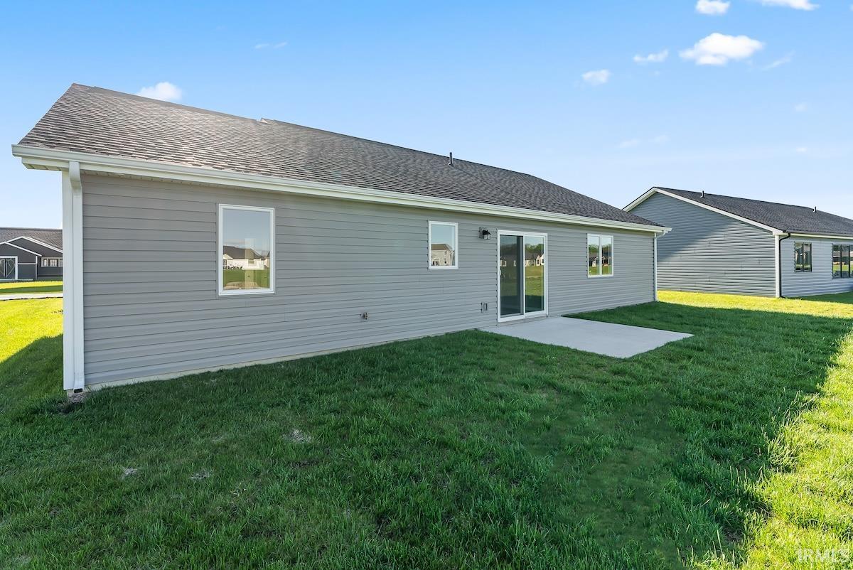 Rear exterior featuring gray horizontal siding, a dark shingled roof, white window trim, and a concrete patio