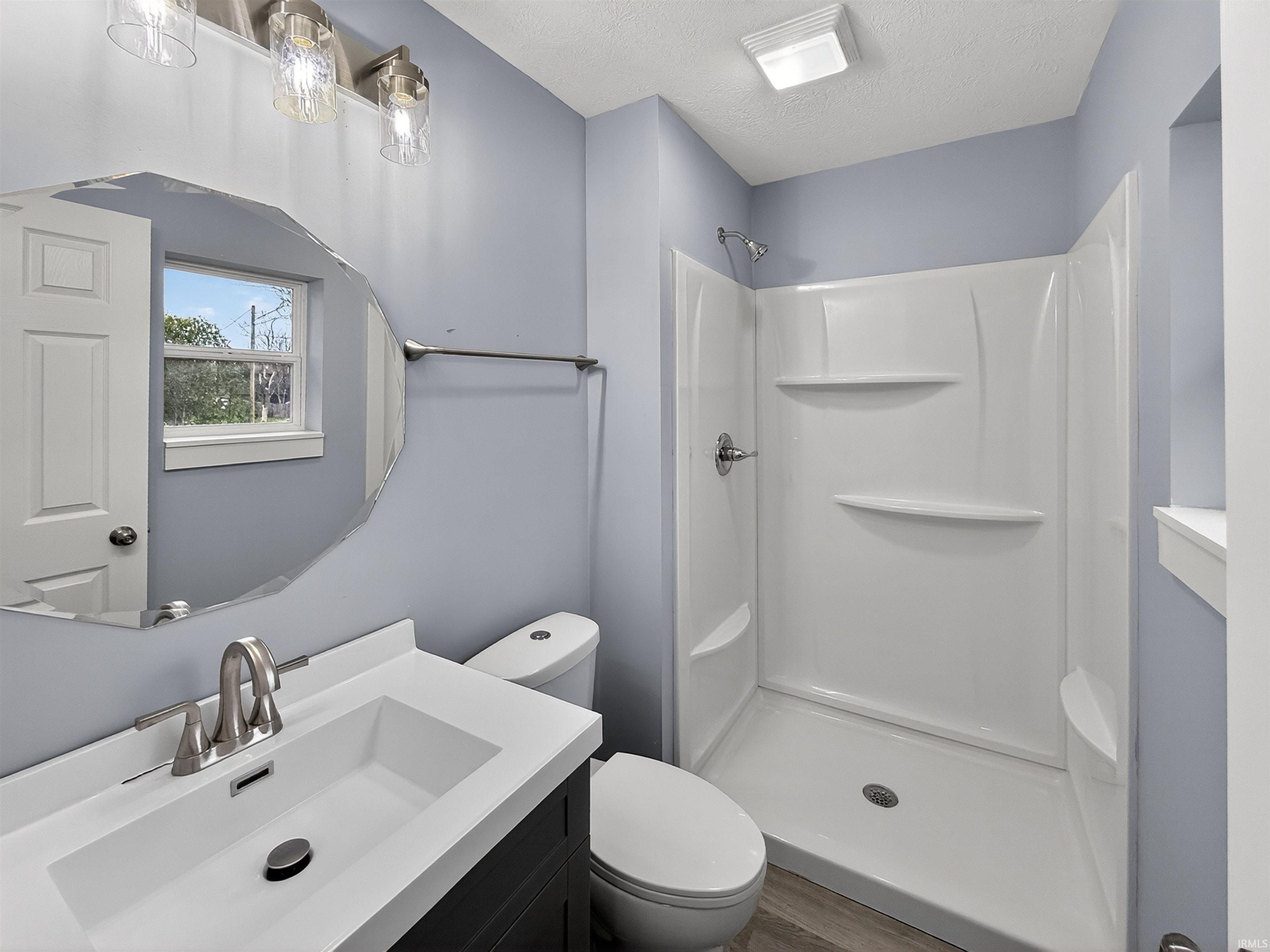 Bathroom featuring a vanity with a white countertop and rectangular sink, a decorative mirror, and a walk-in shower with integrated shelving