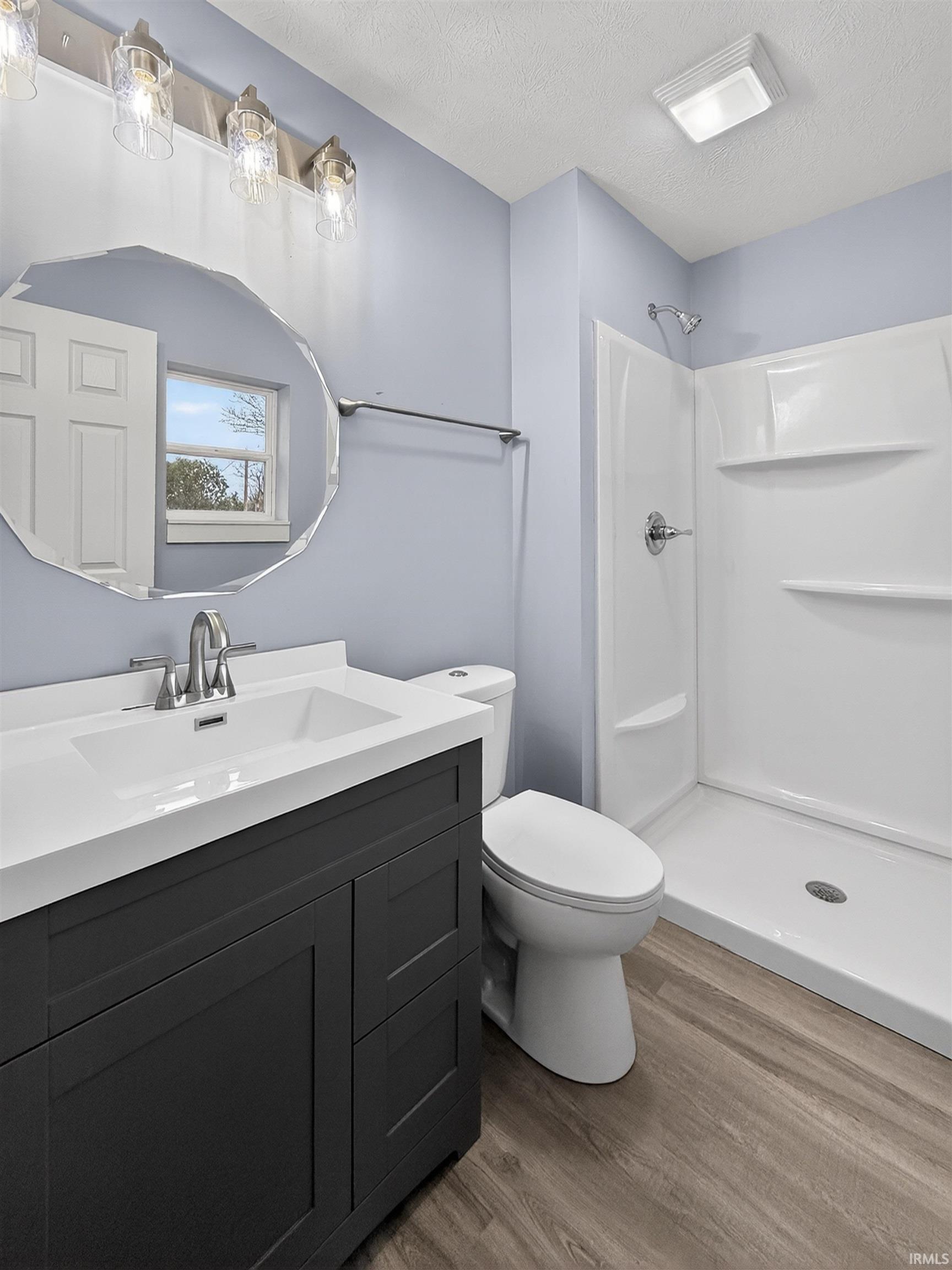 Bathroom featuring a modern dark gray vanity with an integrated white sink and countertop, brushed nickel faucet, and an octagonal mirror