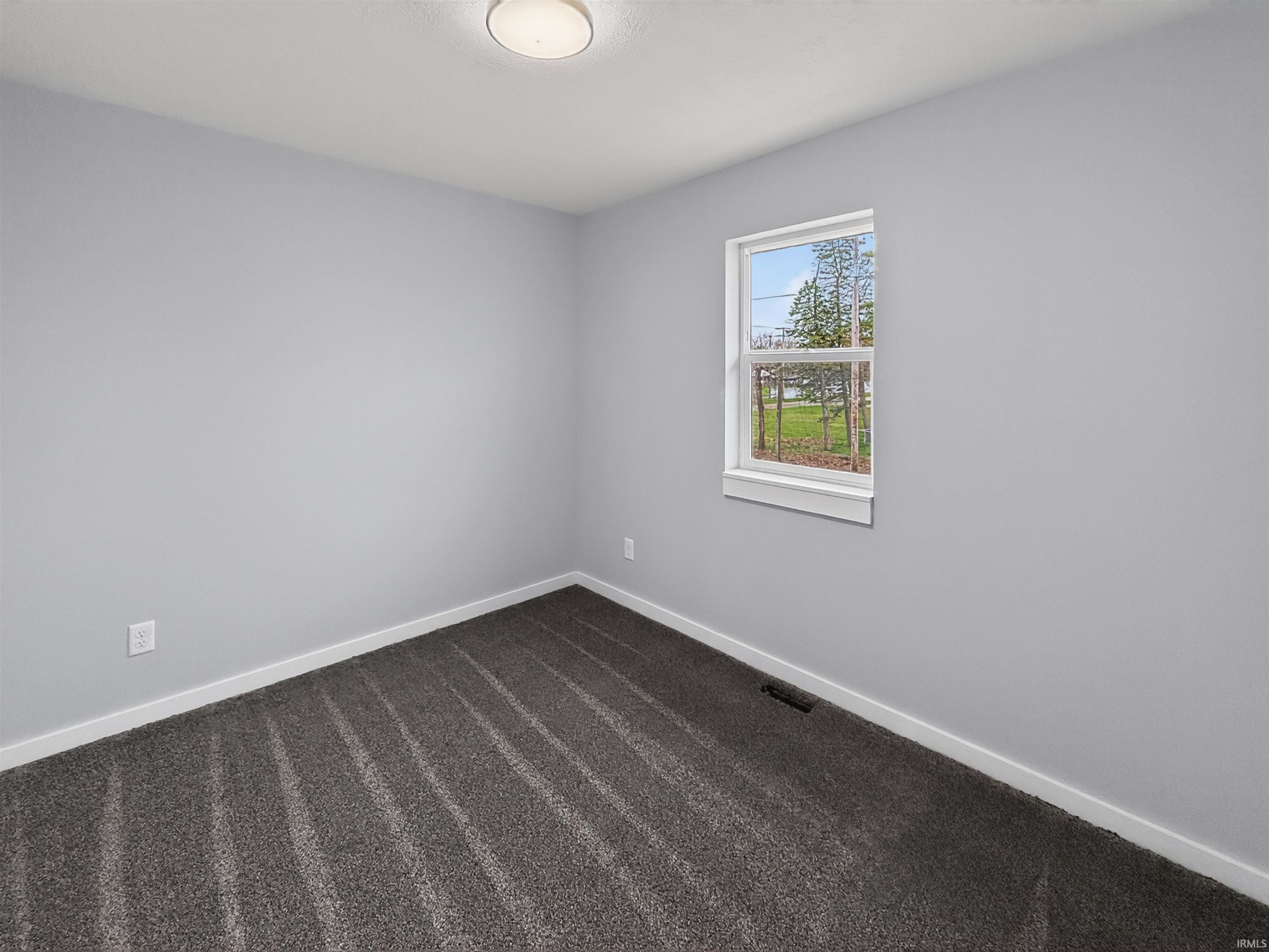 Neutral gray wall paint, dark patterned carpet, white baseboards, and a single window with white trim
