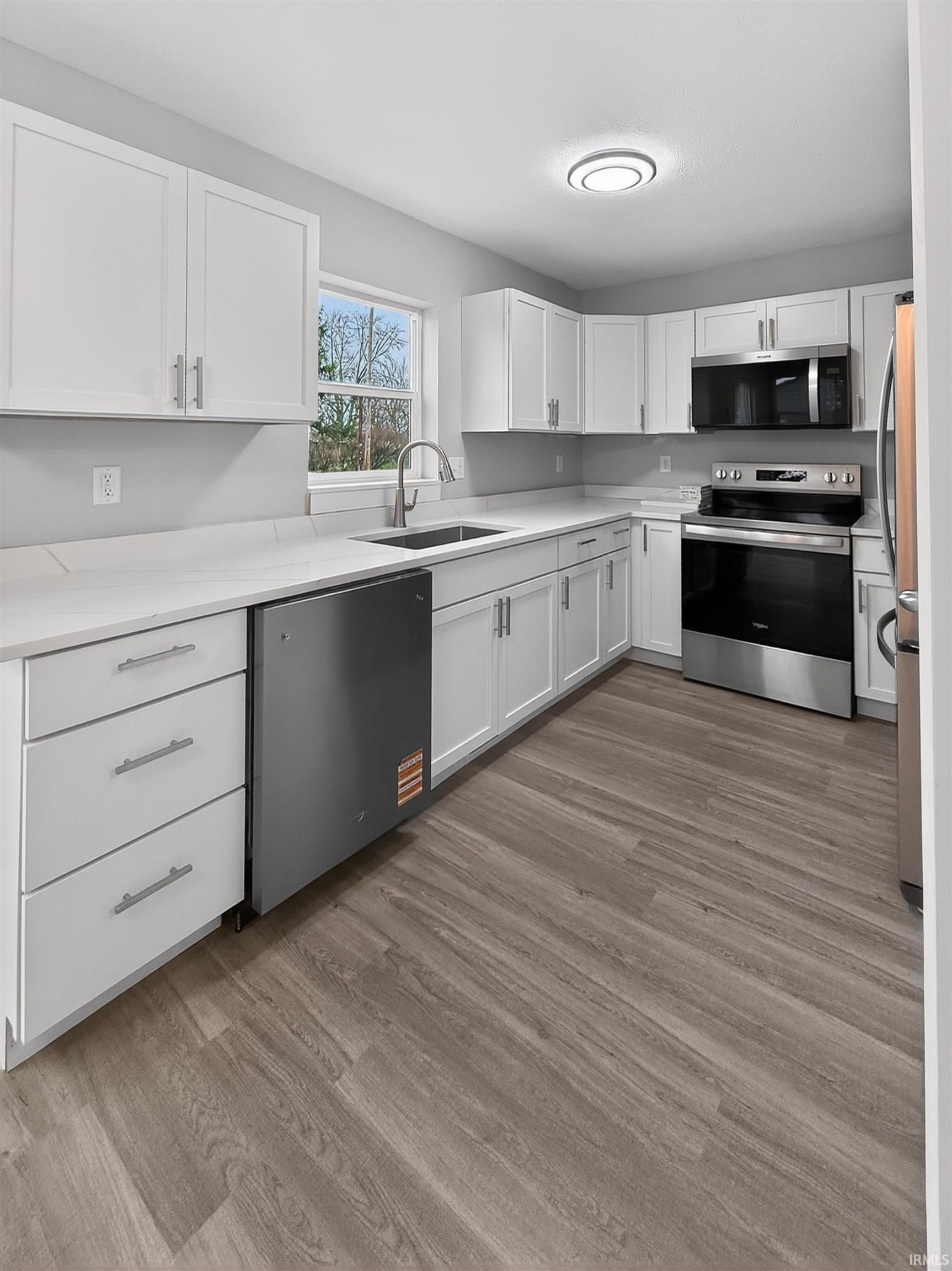 Modern kitchen featuring white cabinetry, stainless steel appliances, light-toned countertops, wood-finish flooring, and a single basin sink with a gooseneck faucet
