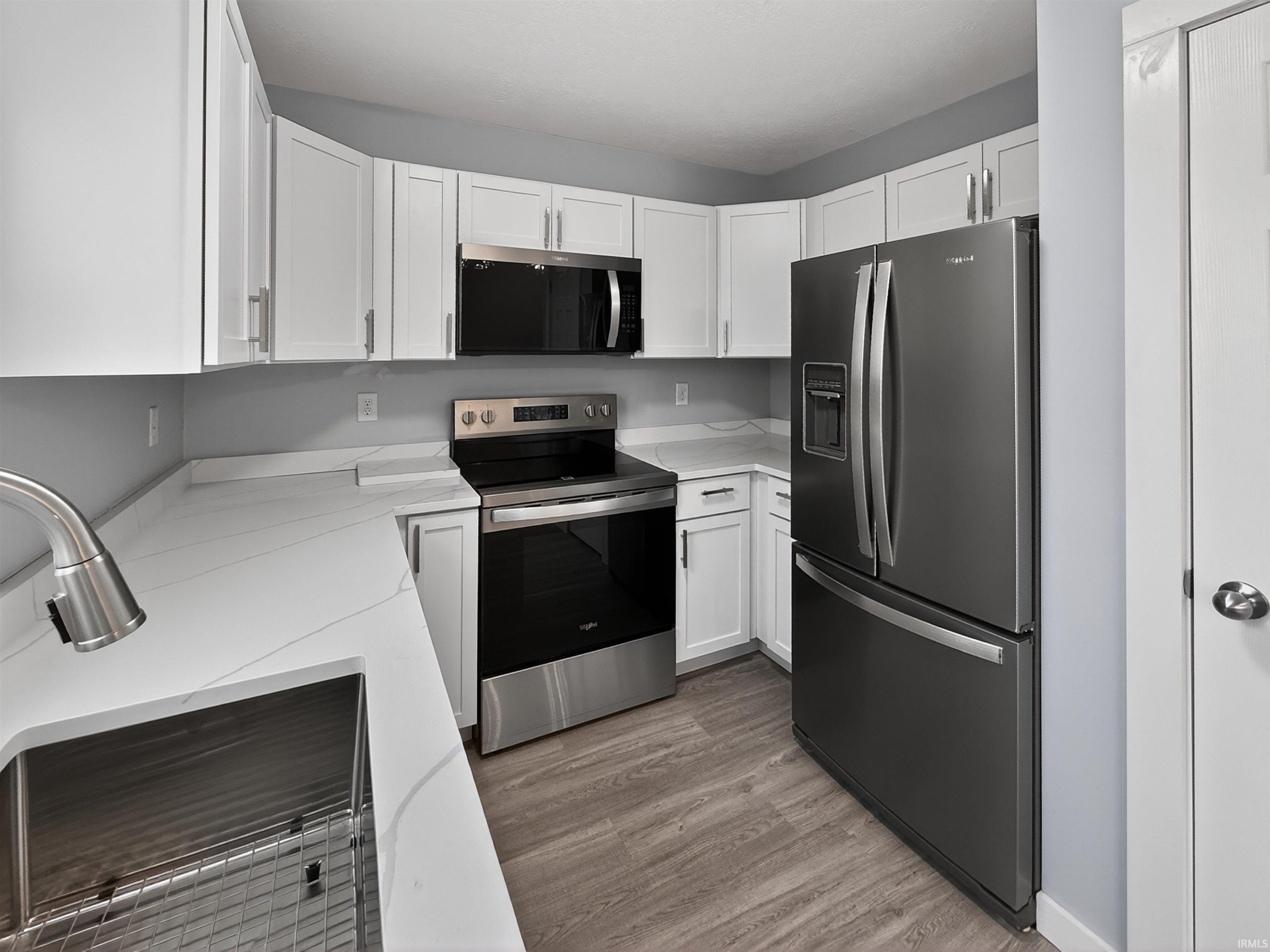 Modern kitchen featuring white cabinetry, light-toned countertops, stainless steel appliances, and wood-finish flooring